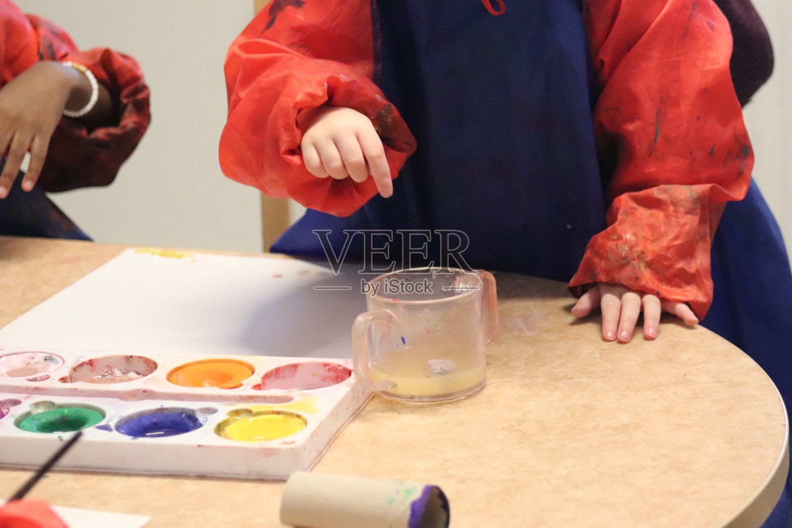 孩子们的手和颜料。幼儿园的绘画课。油漆、水和刷子都在地板上。照片摄影图片