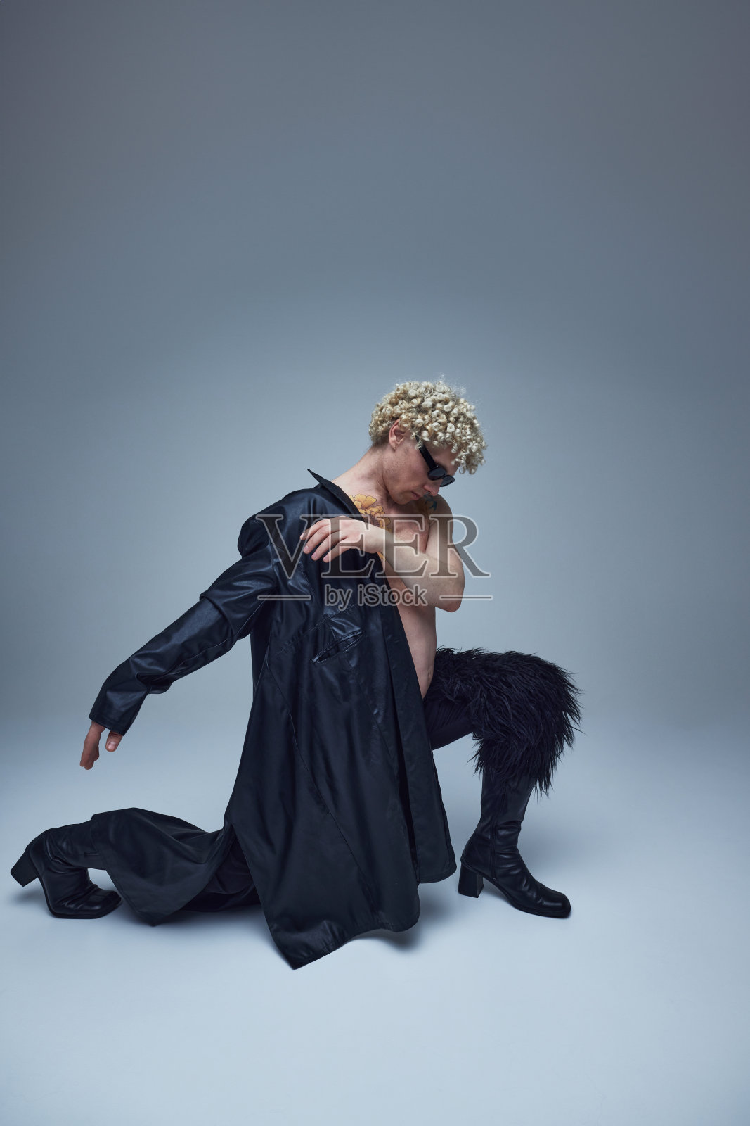 柔韧的男模特表演戏剧性的舞蹈姿势。穿着时髦全黑套装的年轻帅哥在灰色背景下摆姿势。照片摄影图片