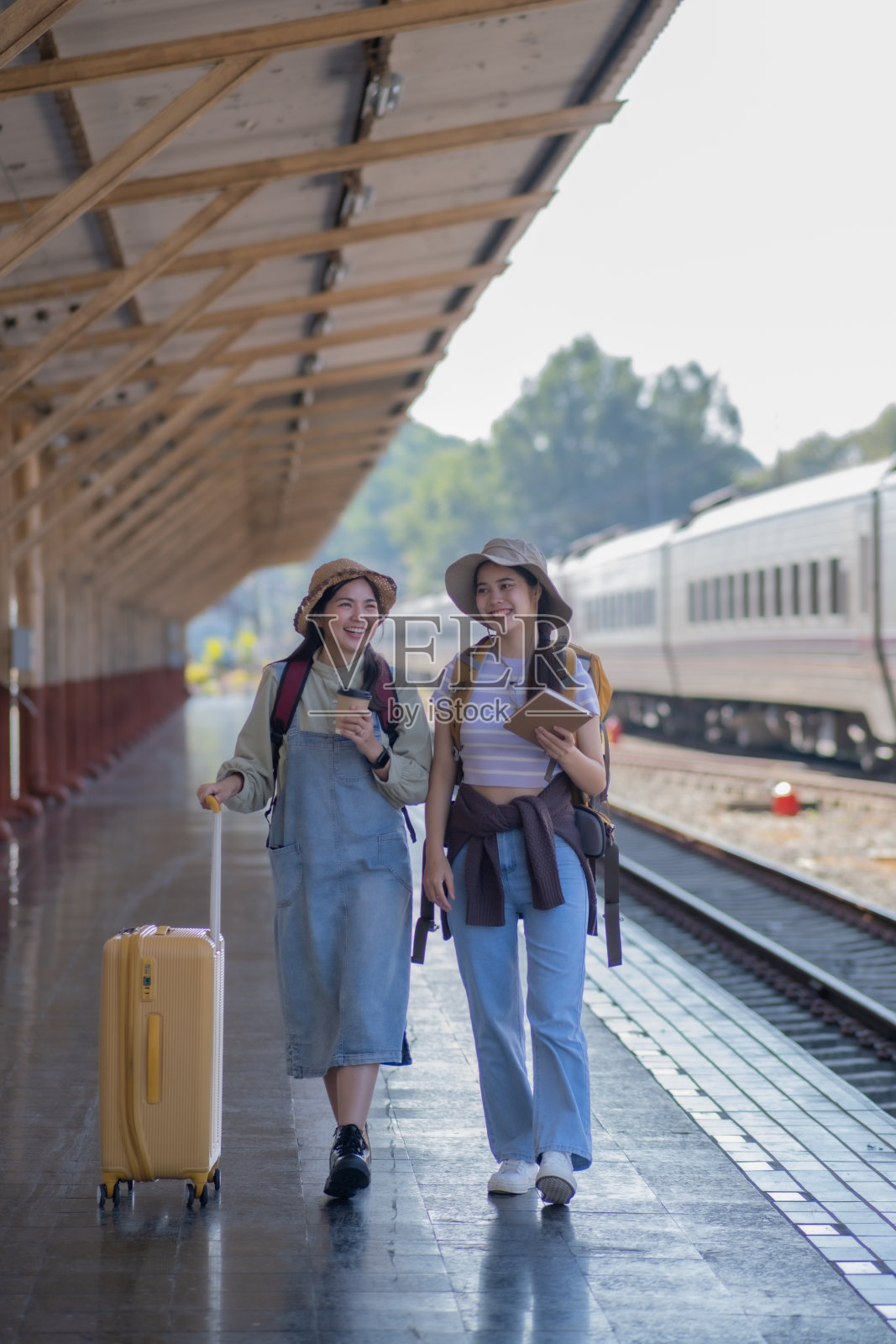 两个年轻的亚洲朋友，背着背包的女孩在火车站等火车，两个美丽的女人在火车站站台上散步照片摄影图片
