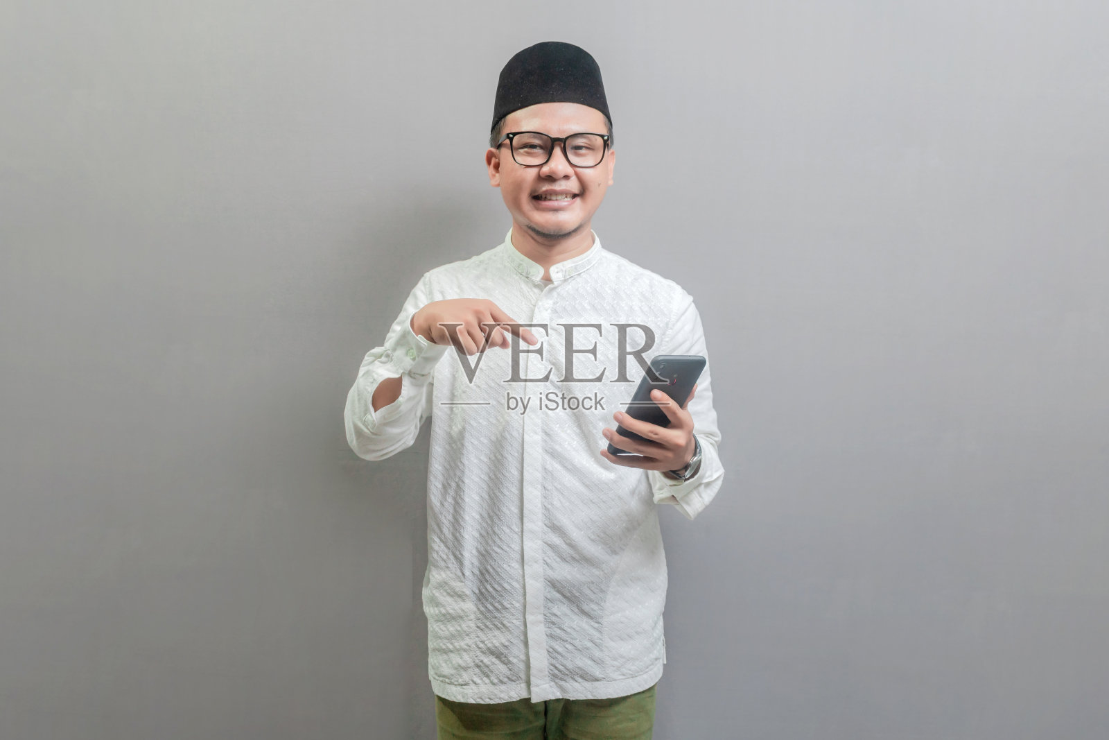 微笑着用手指着智能手机的亚洲穆斯林男子照片摄影图片