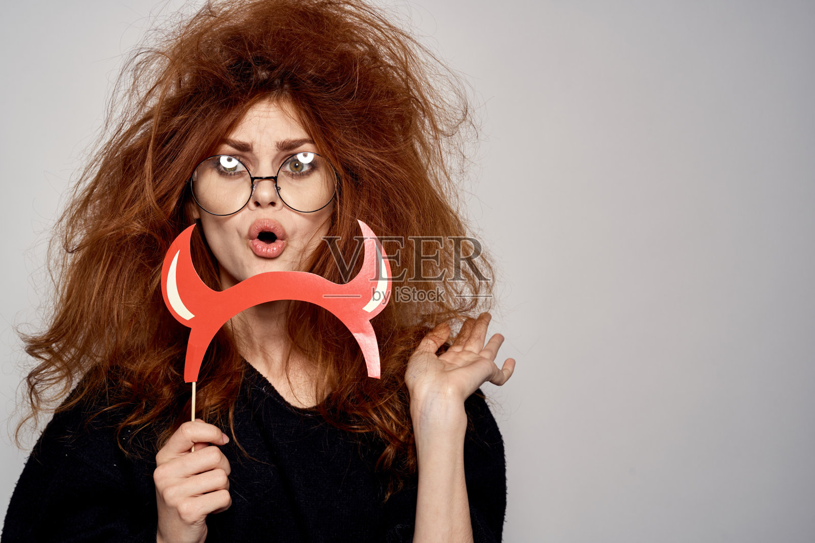 深色头发的女人在万圣节穿着魔鬼服装，红角眼镜，黑裙照片摄影图片