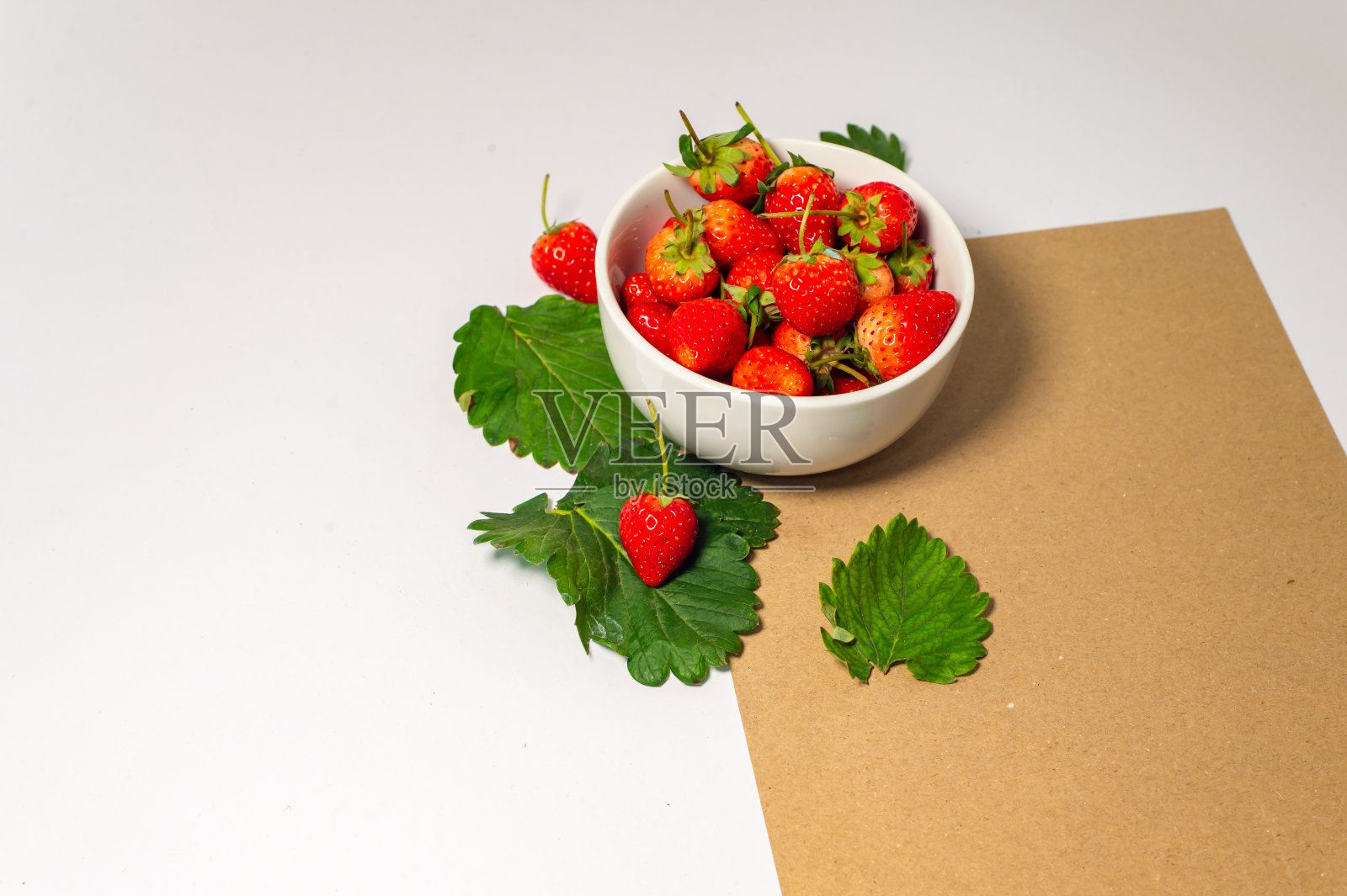 一个装满多汁成熟的红草莓的白色碗。棕色背景草莓，白色桌面，新鲜草莓健康食品图片照片摄影图片