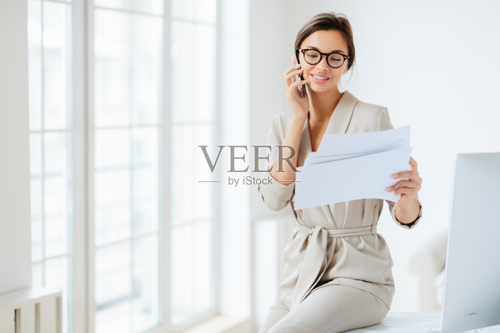 一位面带微笑的女商人在她的办公桌前拿着并检查着一份文件，与人交谈。照片摄影图片