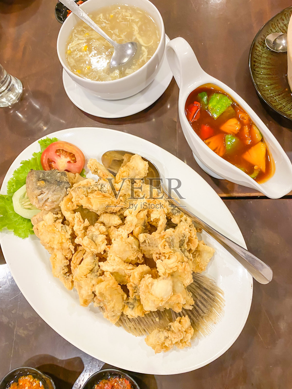 用辣椒酱和蔬菜炒淡水鱼。木桌上的白瓷盘。印度尼西亚的食物和烹饪。美味的油炸美味。照片摄影图片