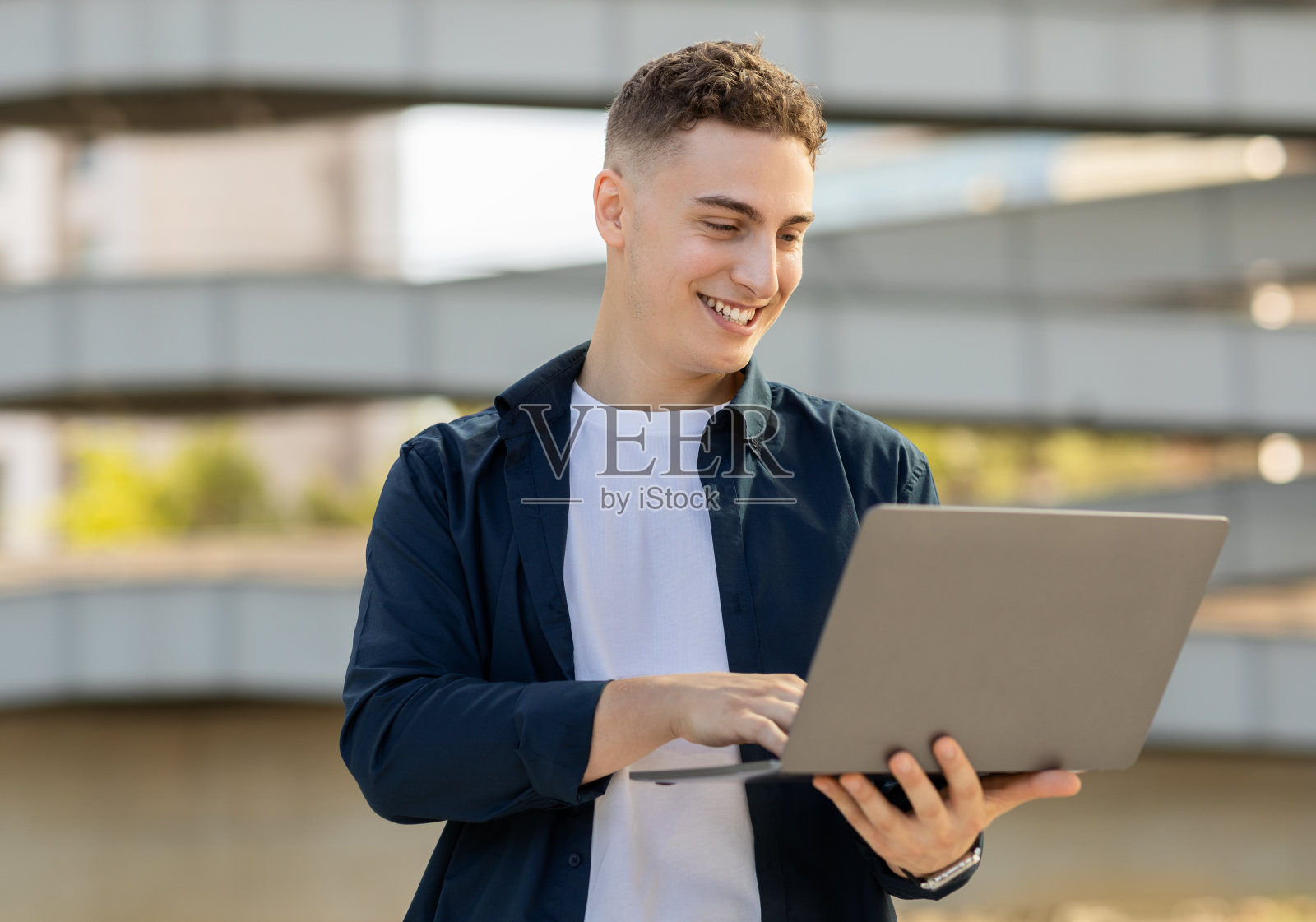 一个穿着便服，在户外使用笔记本电脑的快乐年轻人照片摄影图片