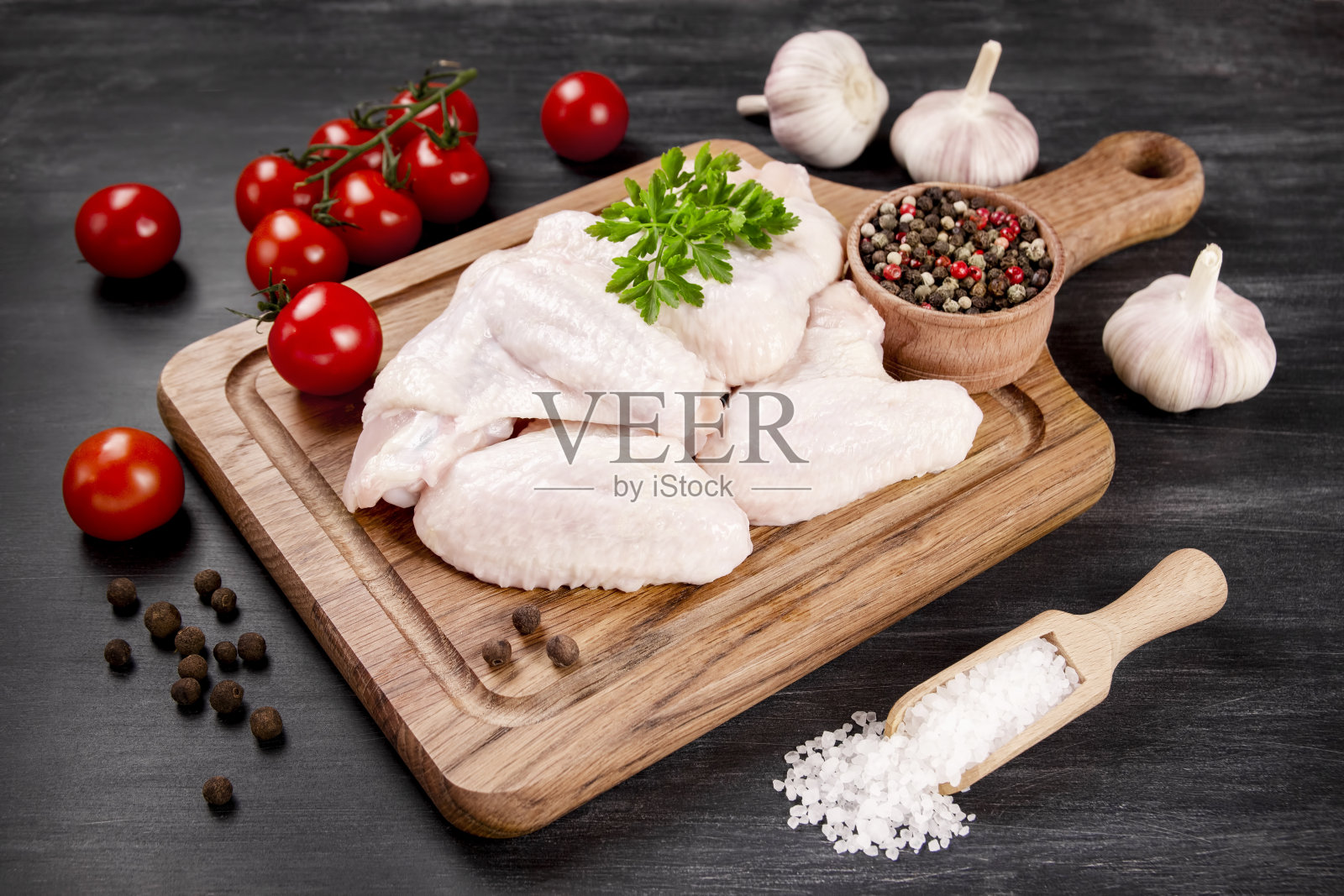 生鸡翅，在深色背景上的木制砧板上有烹饪材料。照片摄影图片