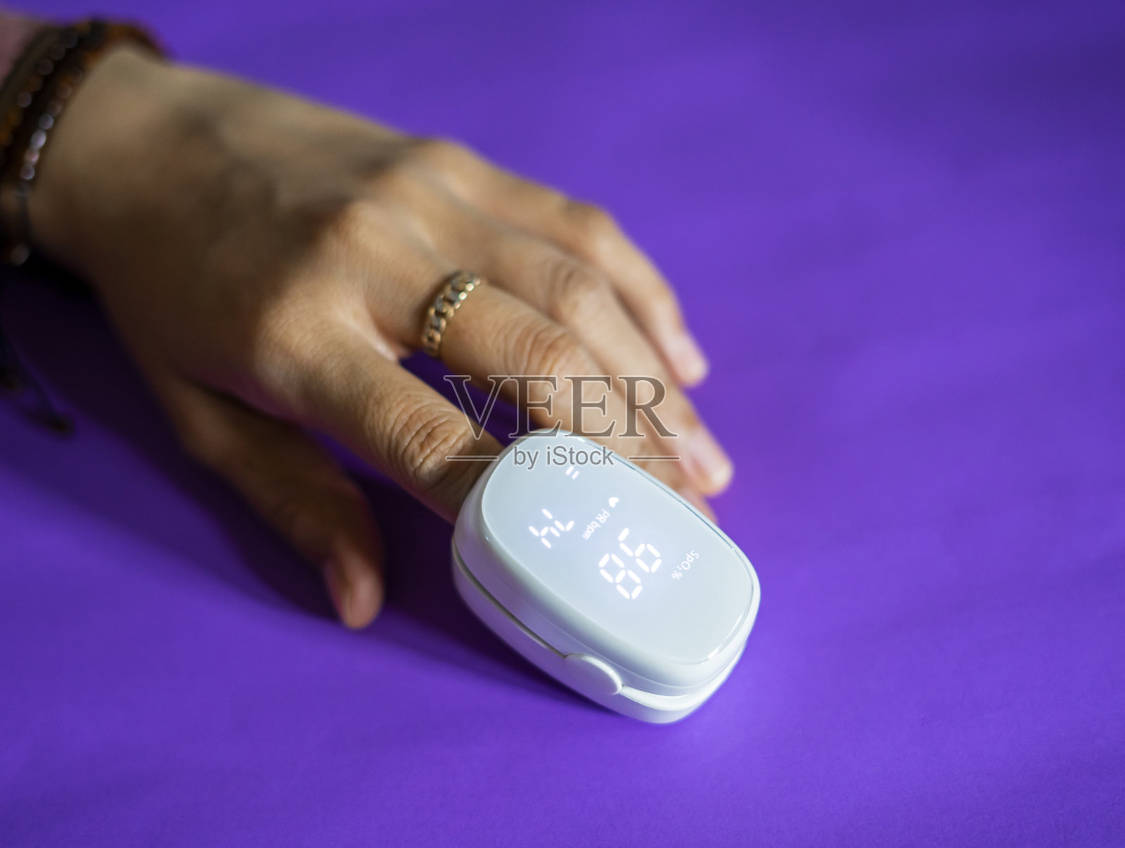 一个女人手指上的脉搏血氧计。一位戴着医用口罩的病人用手指上的电子脉搏血氧计测量血液饱和度。照片摄影图片