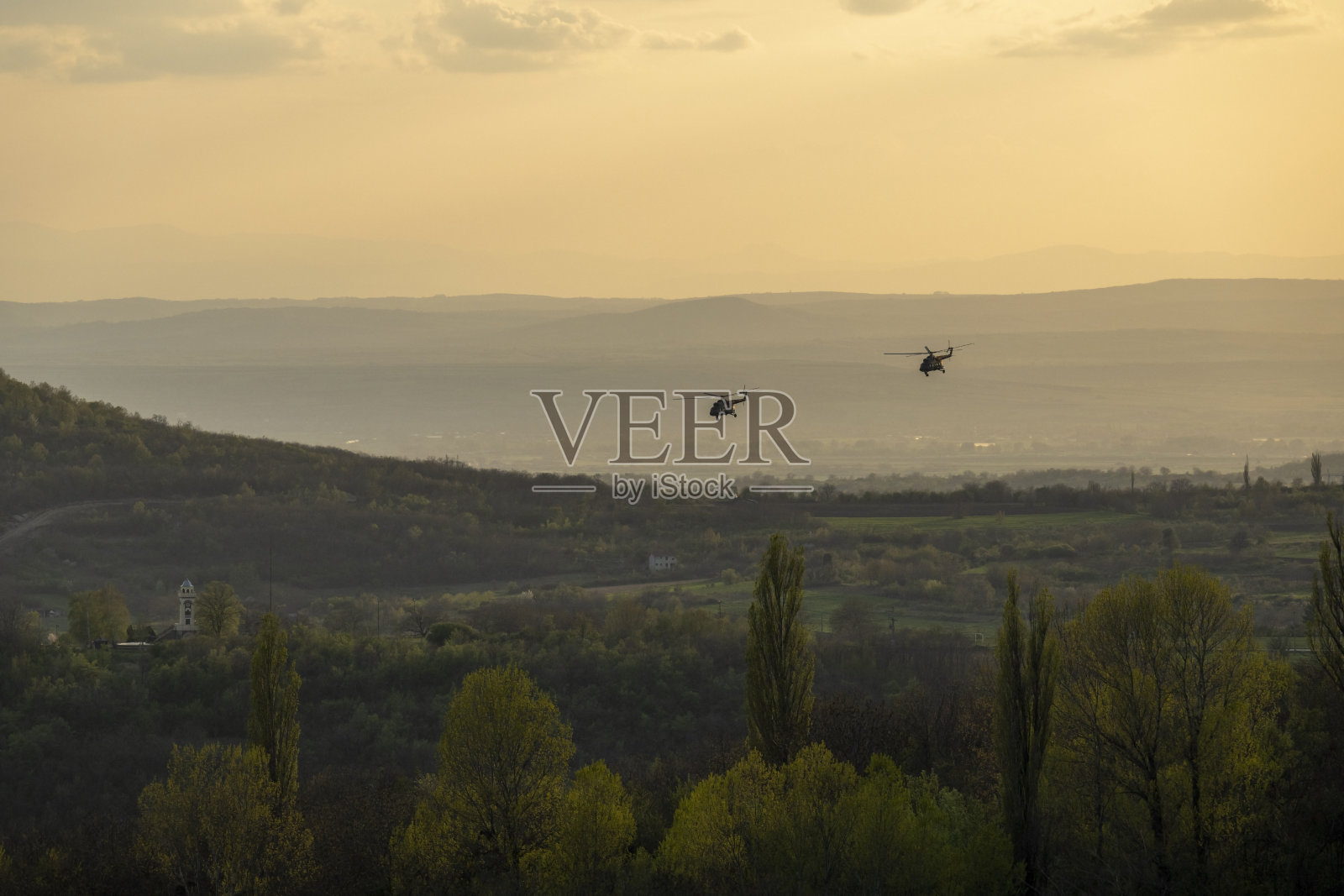 两架直升机飞过田野和森林。照片摄影图片