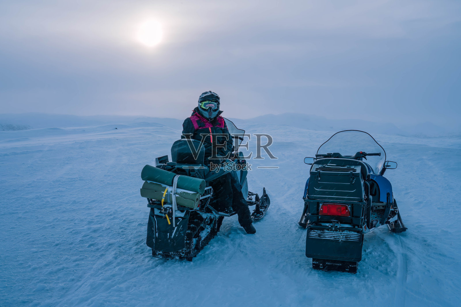 两辆雪地车站在多雪多风的山顶，景色优美。一个人，整体，头盔坐在雪地摩托在照片的右侧，看着相机。瑞典拉普兰照片摄影图片