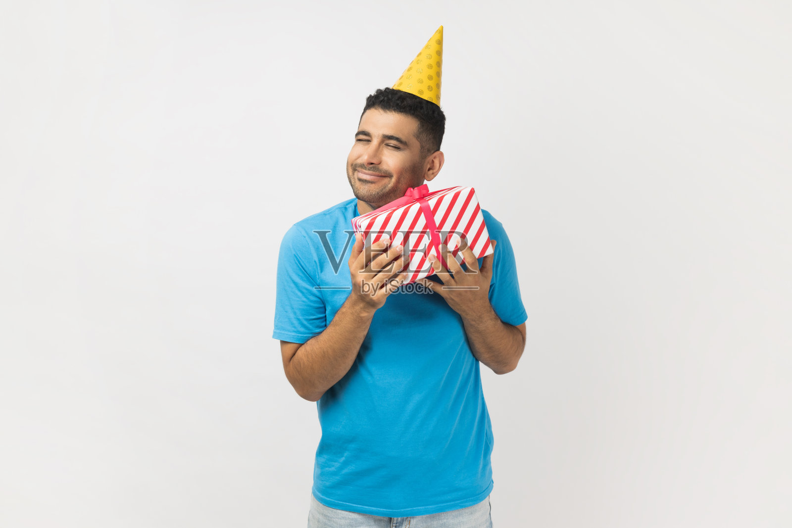 戴着黄色派对帽的微笑男人拥抱他的礼物，拿着礼品盒，高兴地笑着照片摄影图片