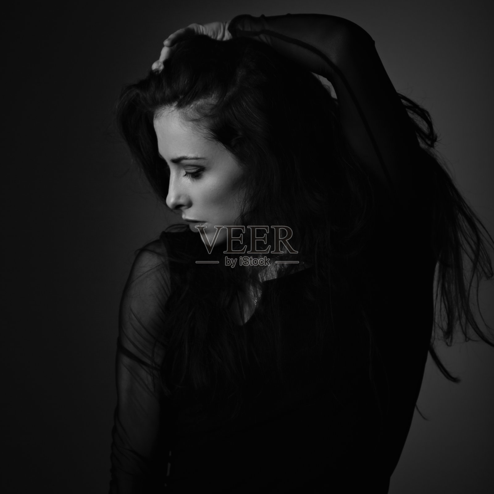 美丽的思考的女人俯视着棕色长发在黑暗的阴影背景。特写肖像照片摄影图片