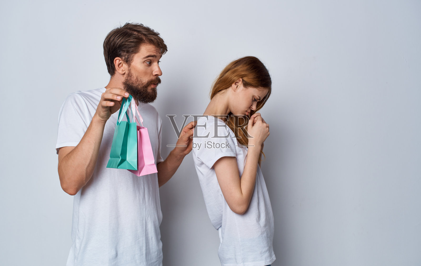 被冒犯的女人转身离开了一个在浅色背景上拿着礼品袋的男人照片摄影图片
