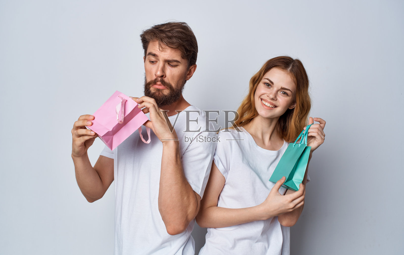 拿着礼品袋的男人和女人背靠背站在灰色背景上照片摄影图片