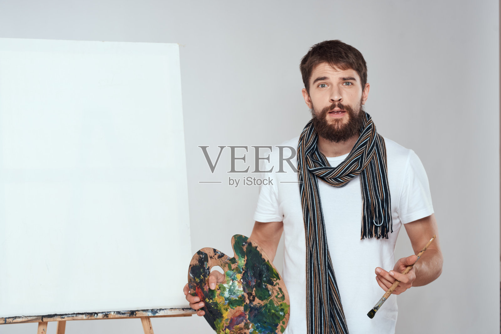 艺术家的调色板和手中的画架艺术爱好围巾围在脖子上一个明亮的背景照片摄影图片