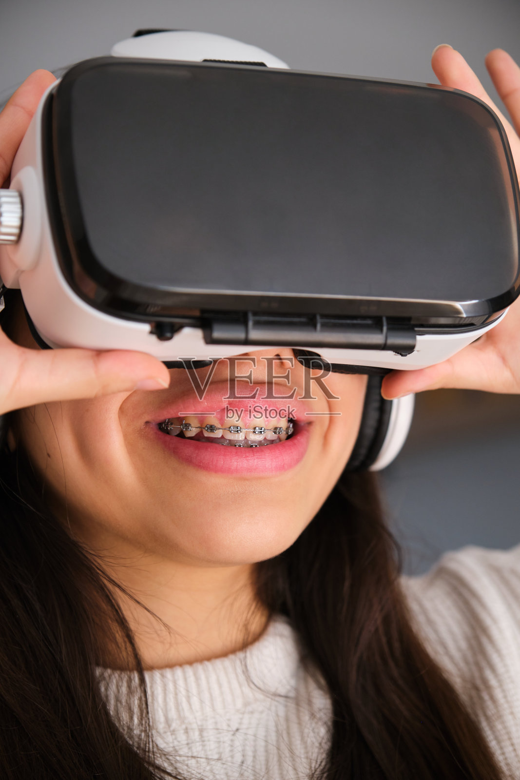 戴着牙套的女青少年在家使用虚拟现实眼镜。照片摄影图片
