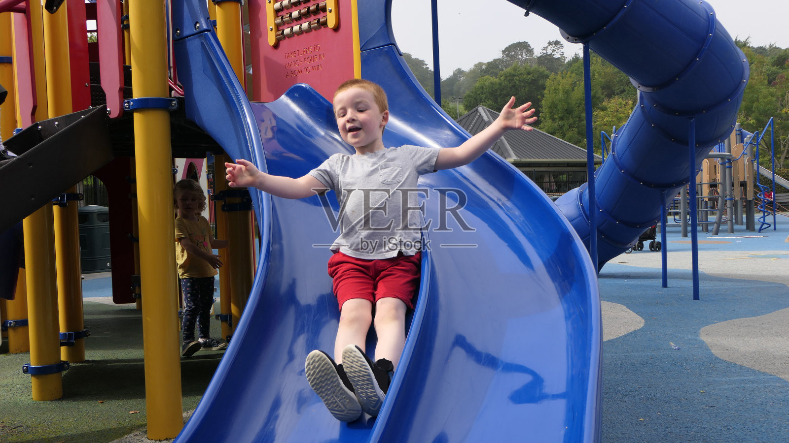 在阳光明媚的日子里，红发男孩在公园里玩滑梯和秋千照片摄影图片