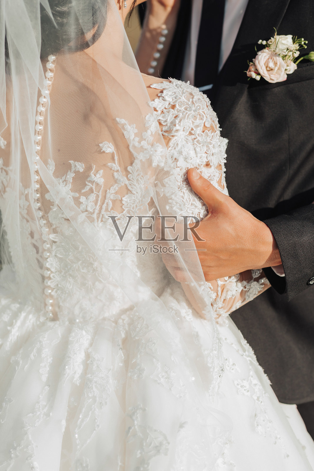 裁剪照片。身穿黑色西装的新郎牵着身穿漂亮蕾丝白色婚纱的新娘的手。美丽的手。肖像。明夏婚礼照片摄影图片