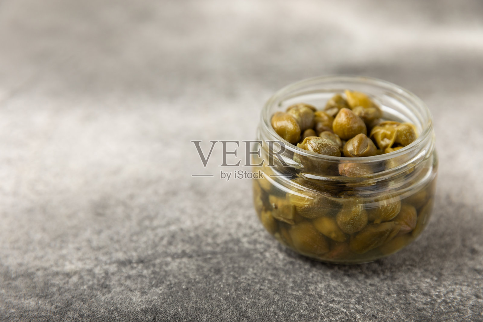 木桌上的玻璃罐子里装着刺山柑。刺山柑加海盐和迷迭香。腌酸豆。地中海菜的食材。有机香料和调味料。副本的空间。照片摄影图片