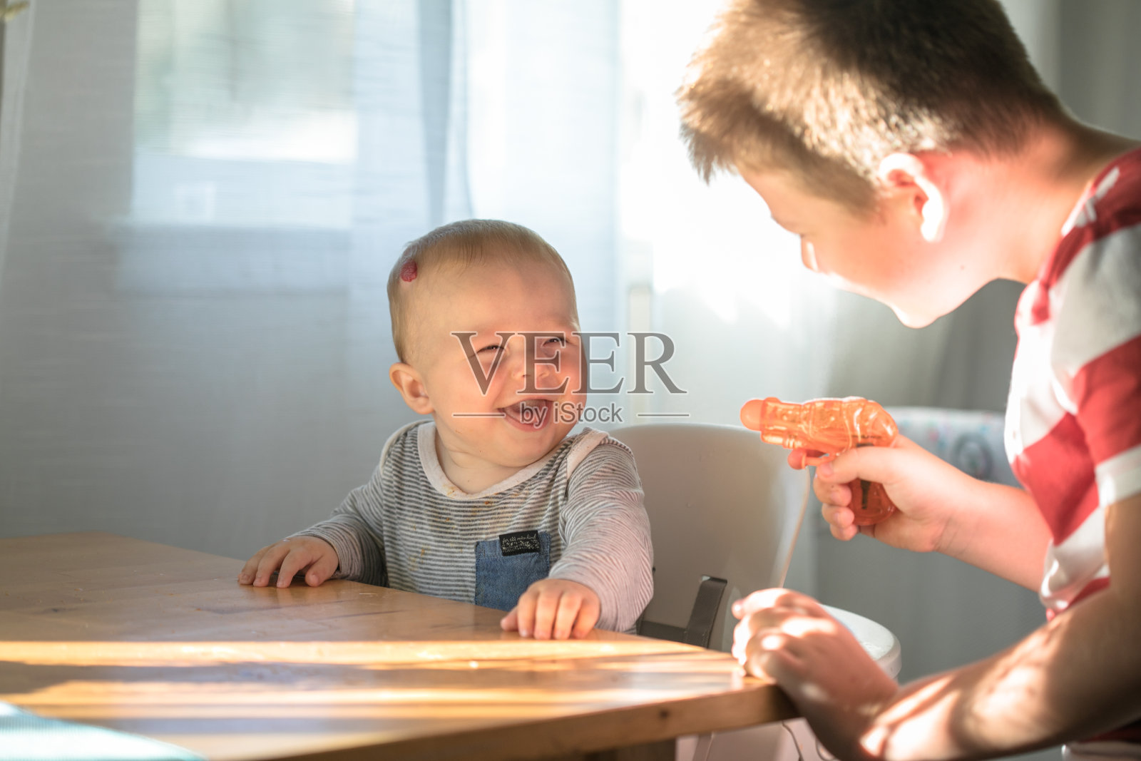 哥哥和他的小男孩玩水枪。两个兄弟姐妹。美丽可爱的家庭在爱，可爱的婴儿和孩子在家里玩，在室内。照片摄影图片