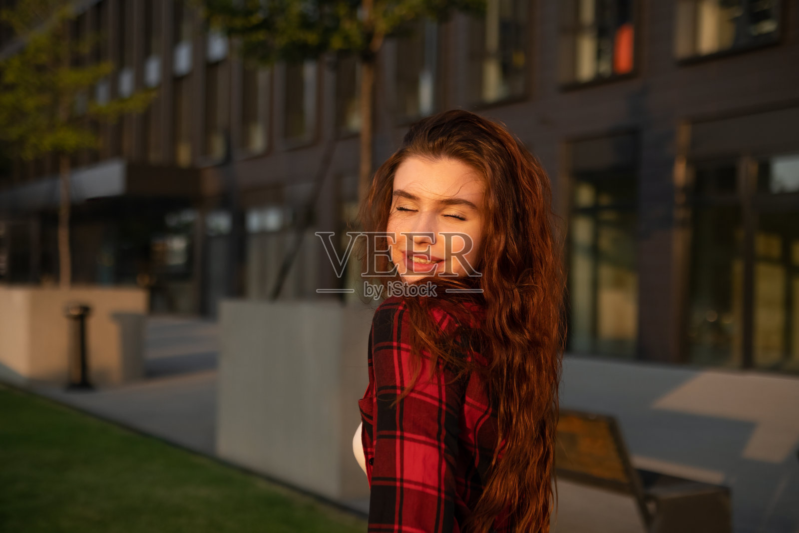 一位红头发、身穿格子衬衫的年轻女子站在那里，脸上带着欢快的微笑。照片摄影图片