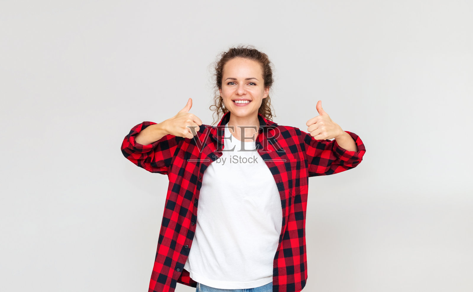 一个快乐自信的年轻女性，在浅灰色的背景前竖起大拇指，微笑着。满足消费者。照片摄影图片