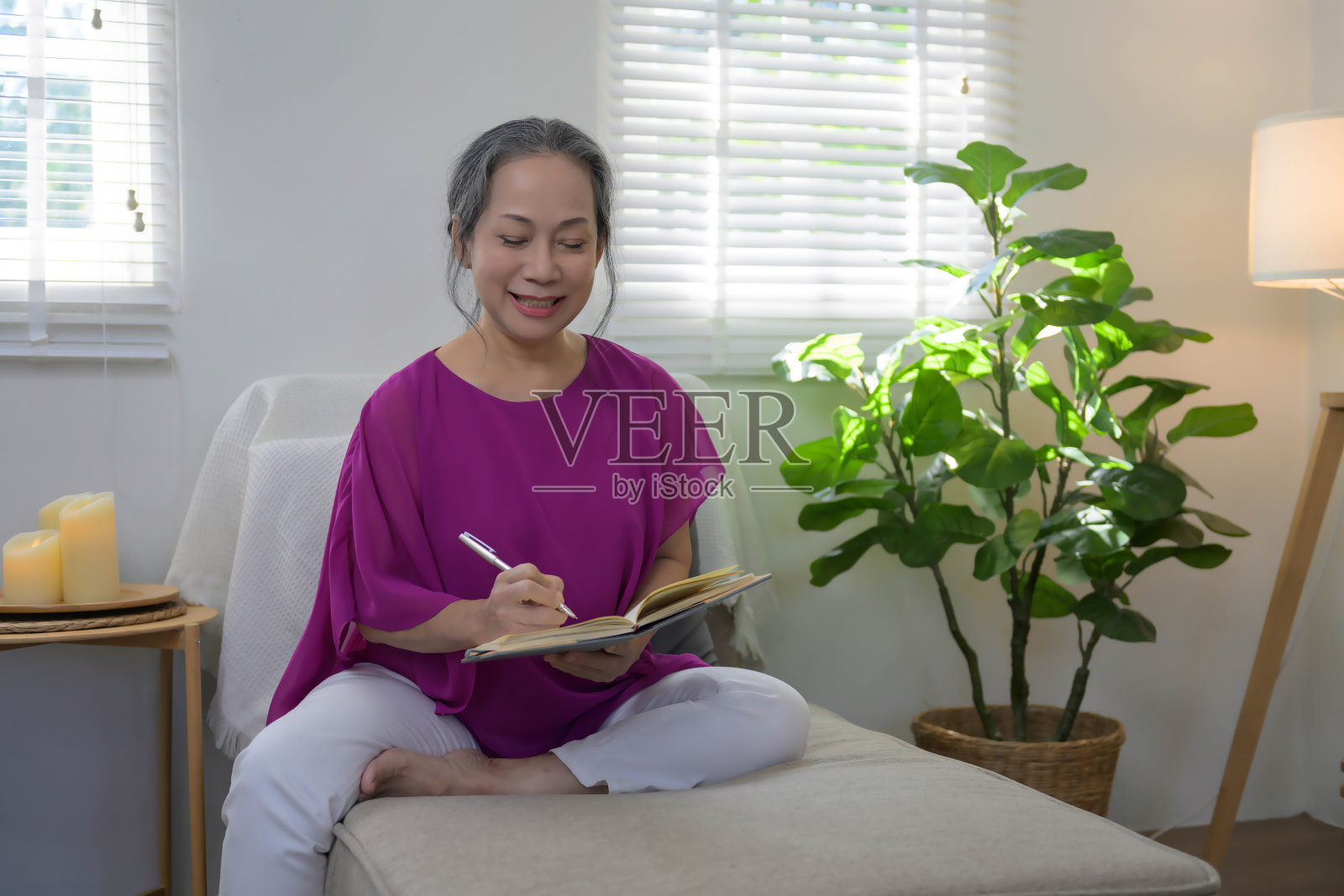 轻松快乐的亚洲老太太坐在客厅的沙发上，在笔记本上写下她的想法。照片摄影图片