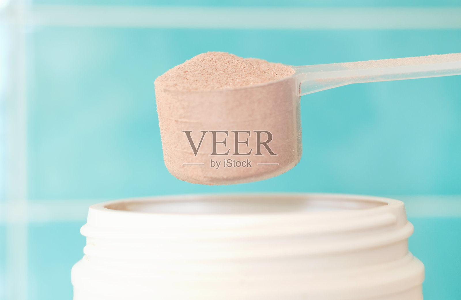 女性的手从罐子里舀出棕色蛋白质，蓝色背景，侧面。照片摄影图片