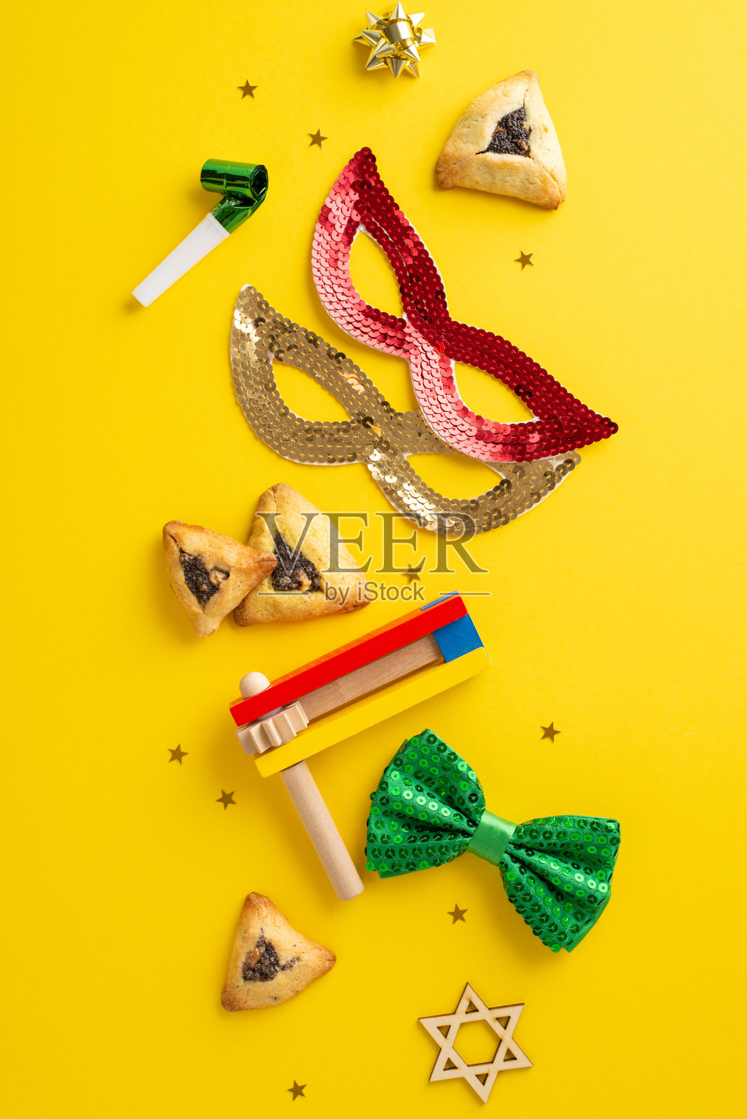 普林节节日布局：俯视垂直拍摄，展示三角形饼干、大卫之星标志、派对舞会面具、领结、五彩纸屑、经典响板，所有这些都以鲜艳的黄色为背景照片摄影图片