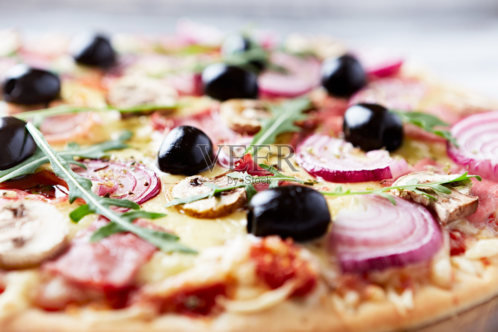 披萨配火腿，香菇，马苏里拉奶酪，黑橄榄和新鲜rucola木制背景。关闭了。照片摄影图片