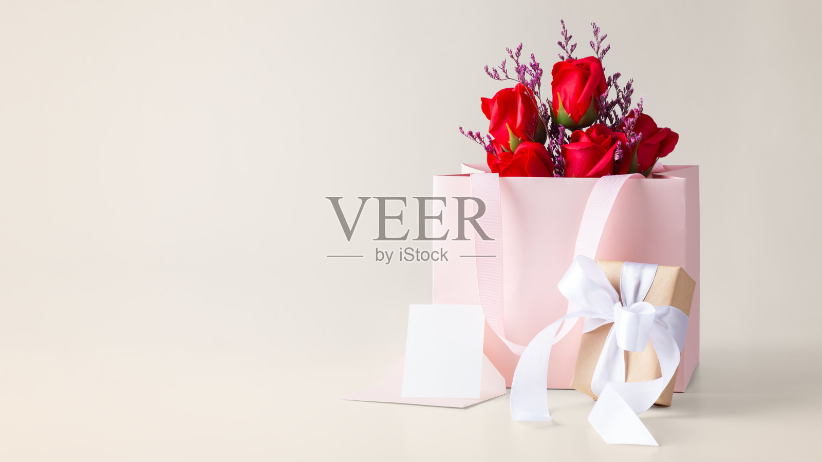 玫瑰花束在纸袋与礼盒和卡片在米色背景照片摄影图片