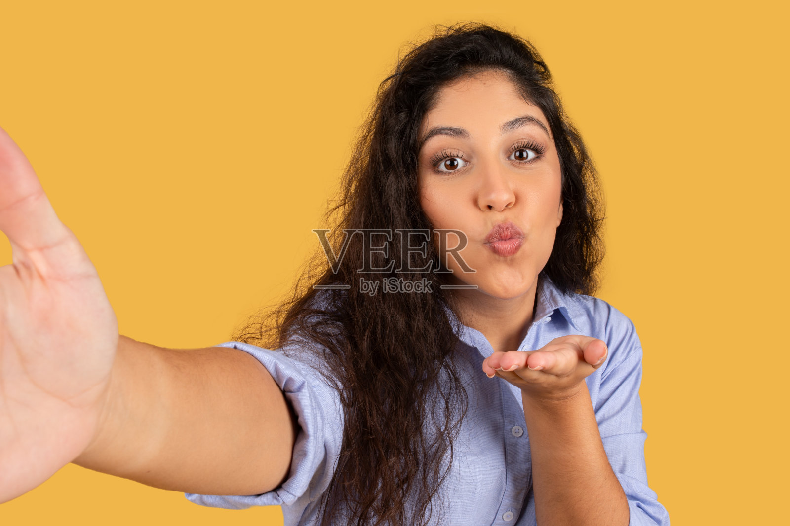 快乐的拉丁年轻黑发女子在不经意间对着手机飞吻，自拍照片摄影图片