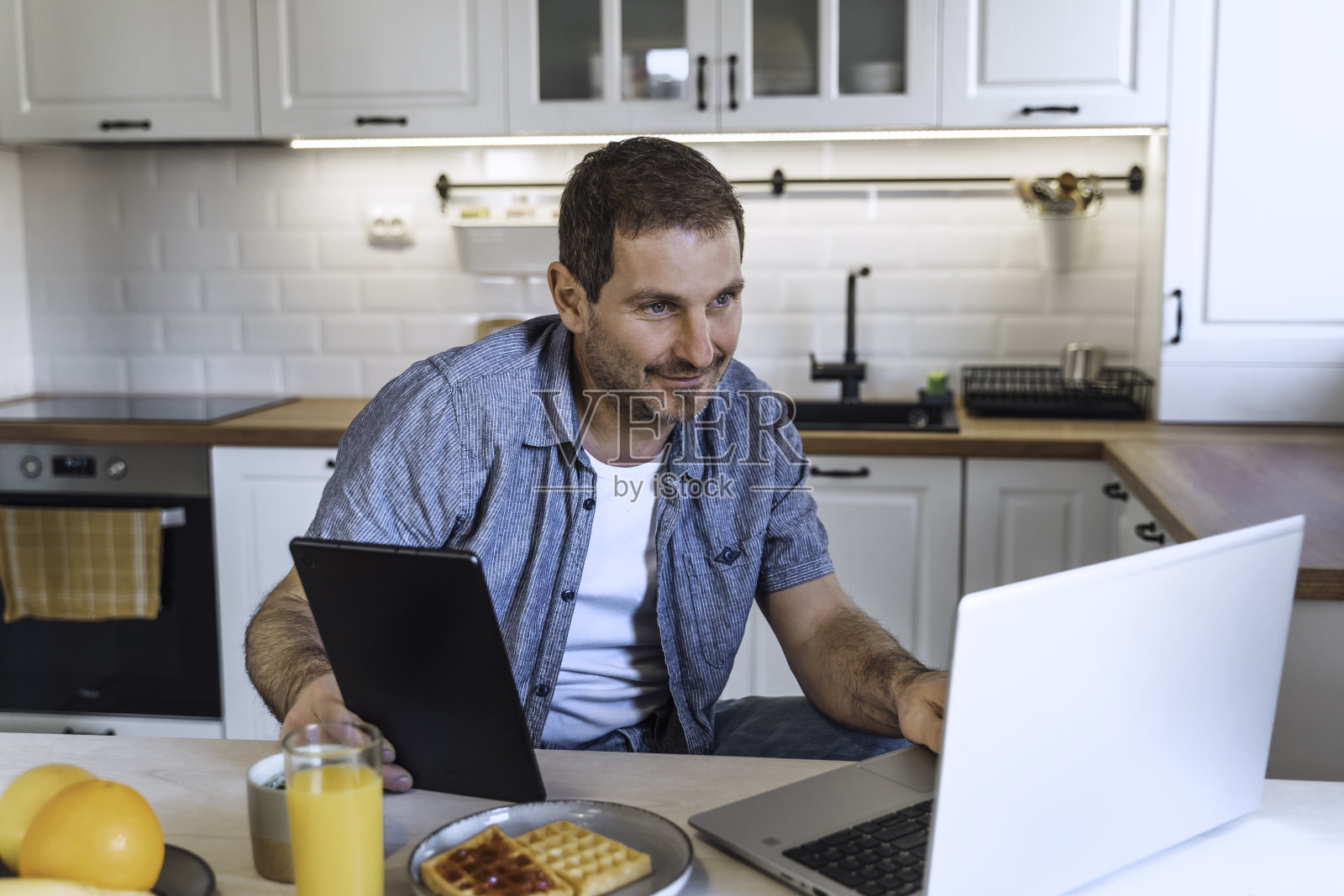 男人在厨房餐桌上吃早餐时使用笔记本电脑照片摄影图片