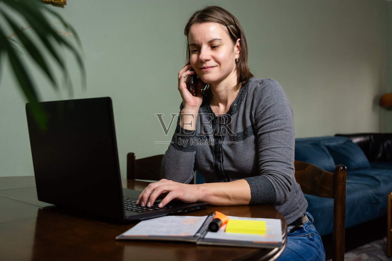 中年成年妇女在家庭办公室用笔记本电脑工作时，正在讲手机。照片摄影图片