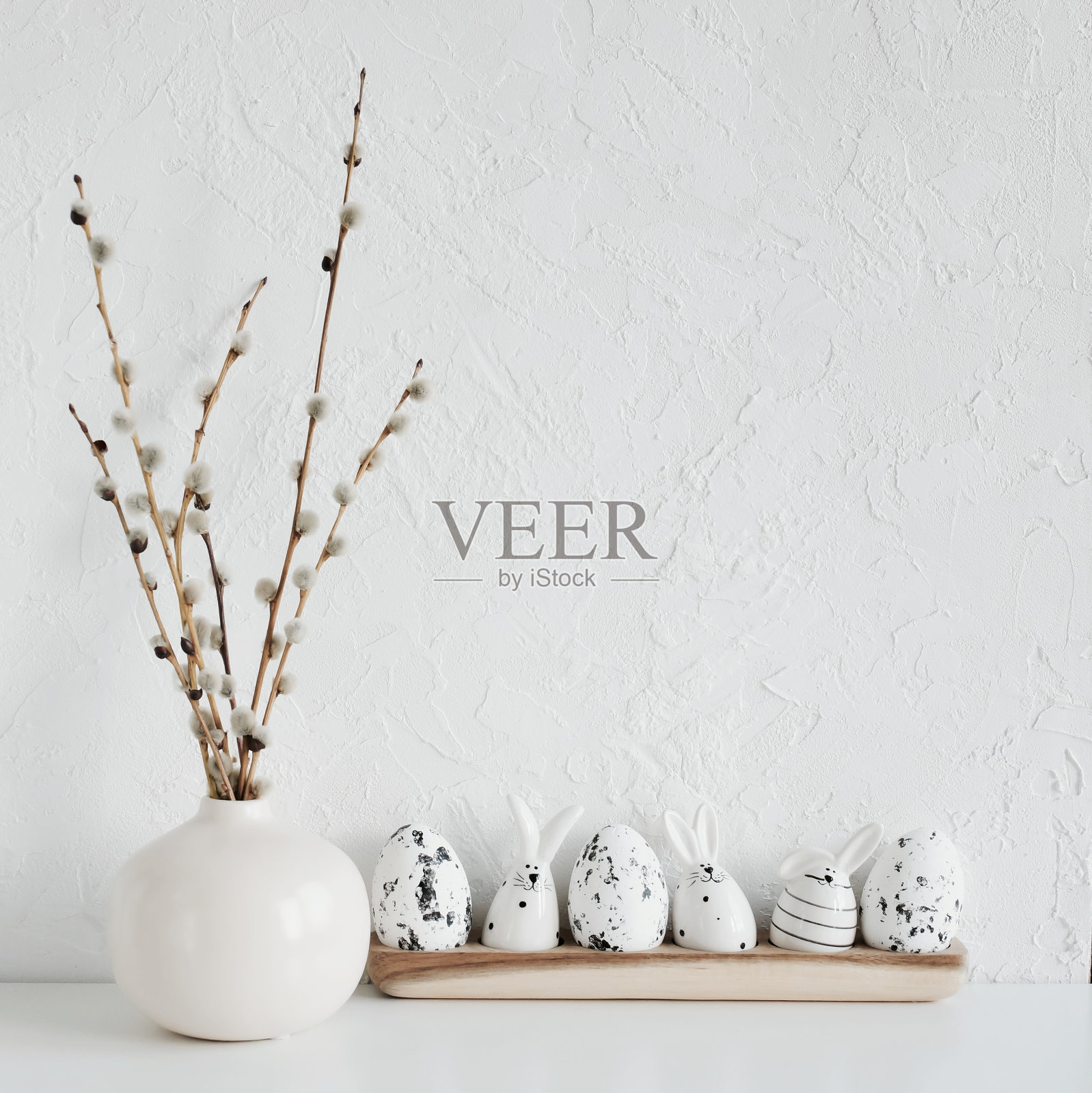 复活节的背景。春天的柳枝在花瓶和复活节彩蛋和有趣的兔子装饰在白色纹理墙在中性色。本空间照片摄影图片