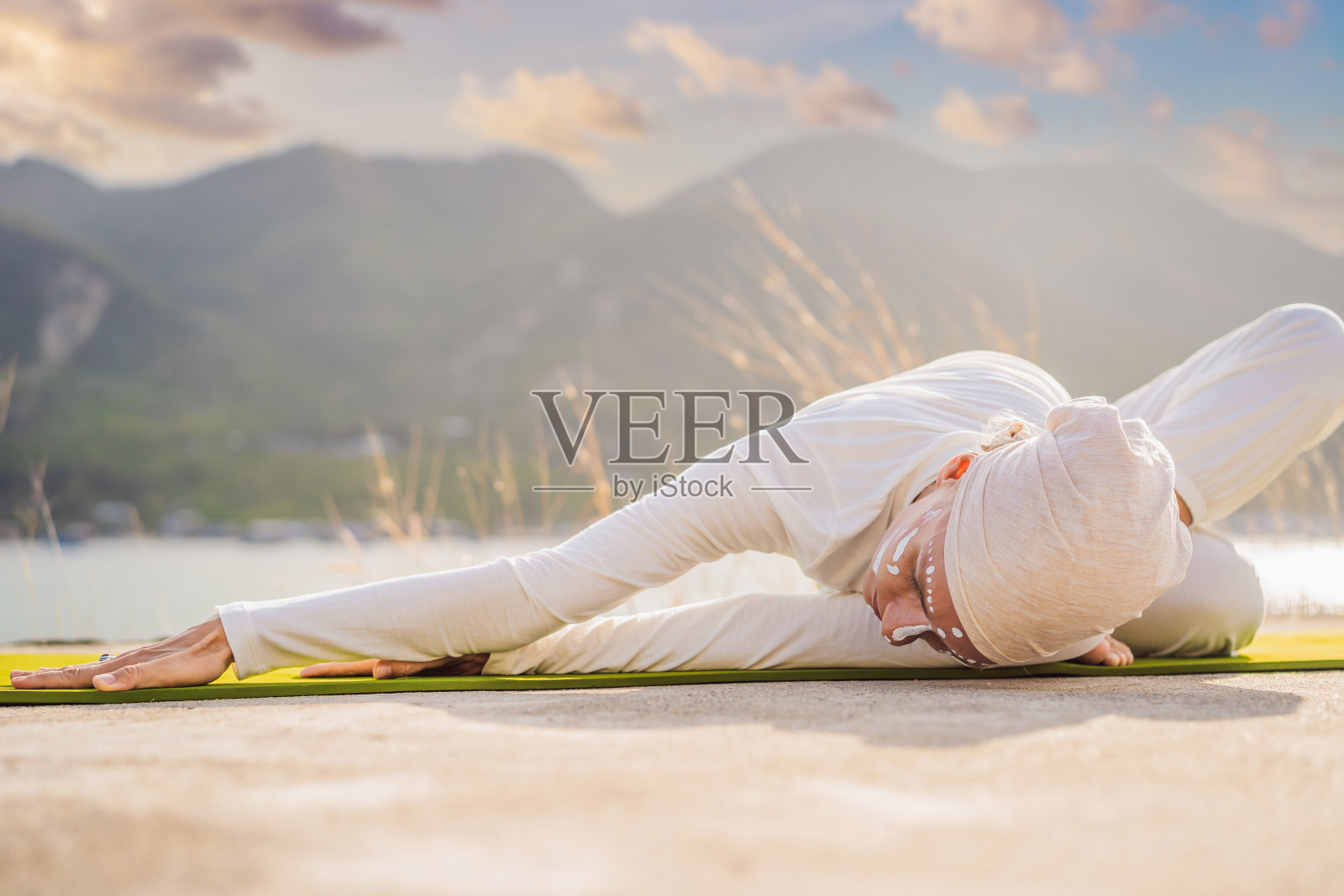 昆达里尼瑜伽女子穿着白色的衣服，戴着头巾，在大海、山脉和日落的背景下练习昆达里尼瑜伽。印第安人的战斗脸画展示了她的内心世界。一个致力于瑜伽的女人的视觉故事照片摄影图片