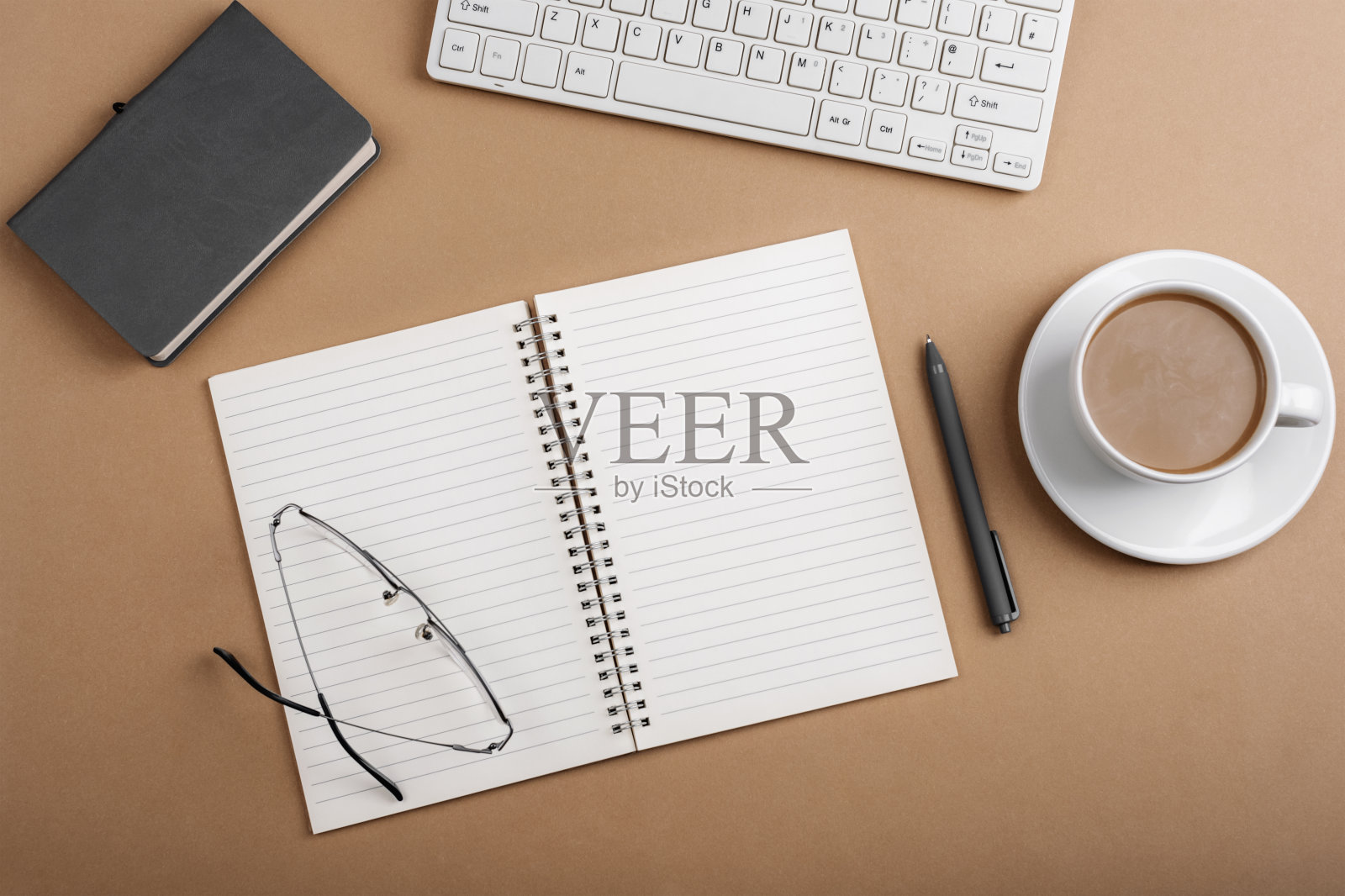 桌面有空白的记事本，键盘，眼镜和咖啡杯在棕色的桌子上。俯视图，平铺照片摄影图片