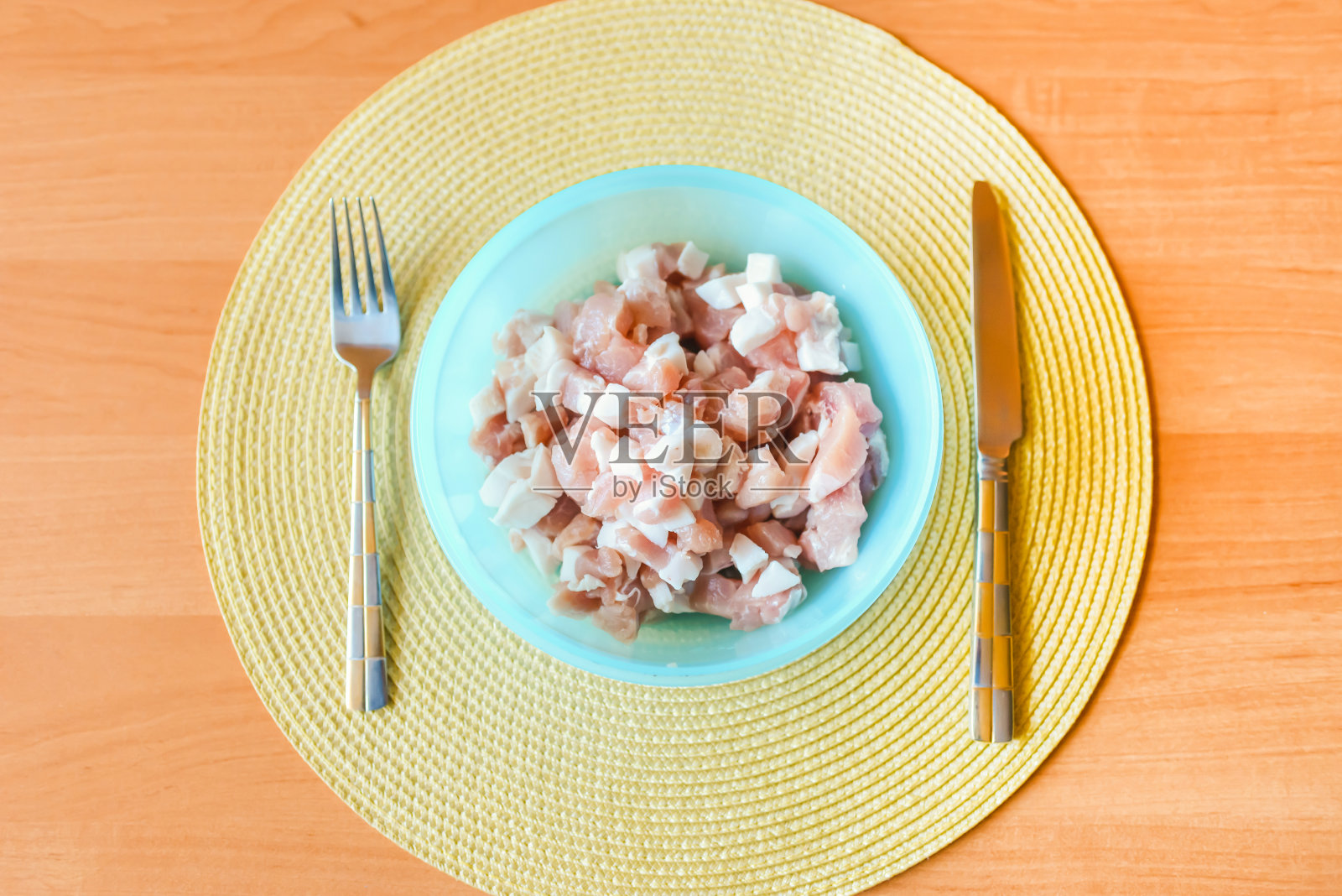 每年的5月6日是国际无饮食日。生切肉猪肉块放在蓝色的碗里放在桌子上，旁边放着刀叉。俯视图，选择性聚焦。照片摄影图片