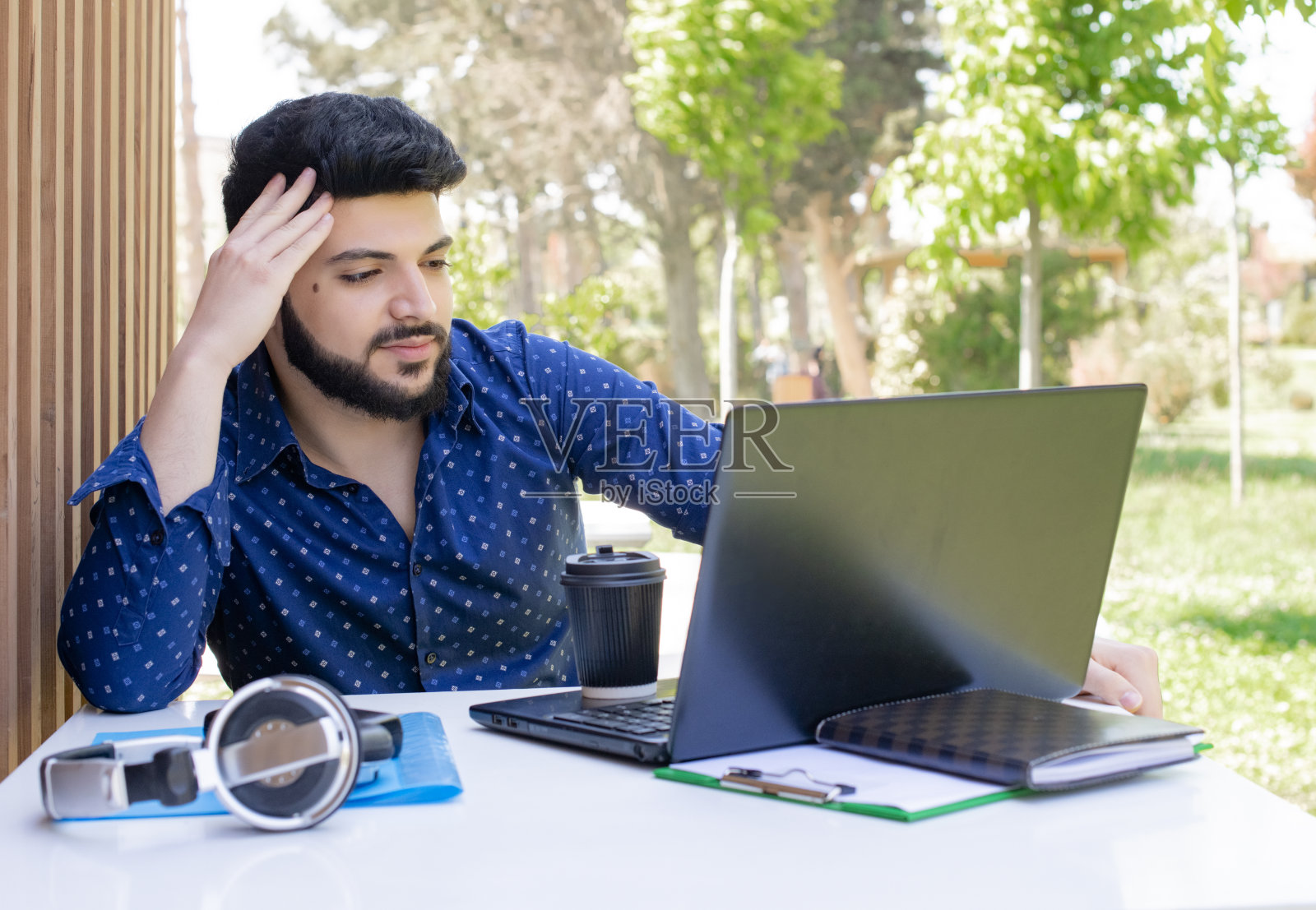 穿着蓝色衬衫的年轻商人坐在桌旁，在户外工作。照片摄影图片