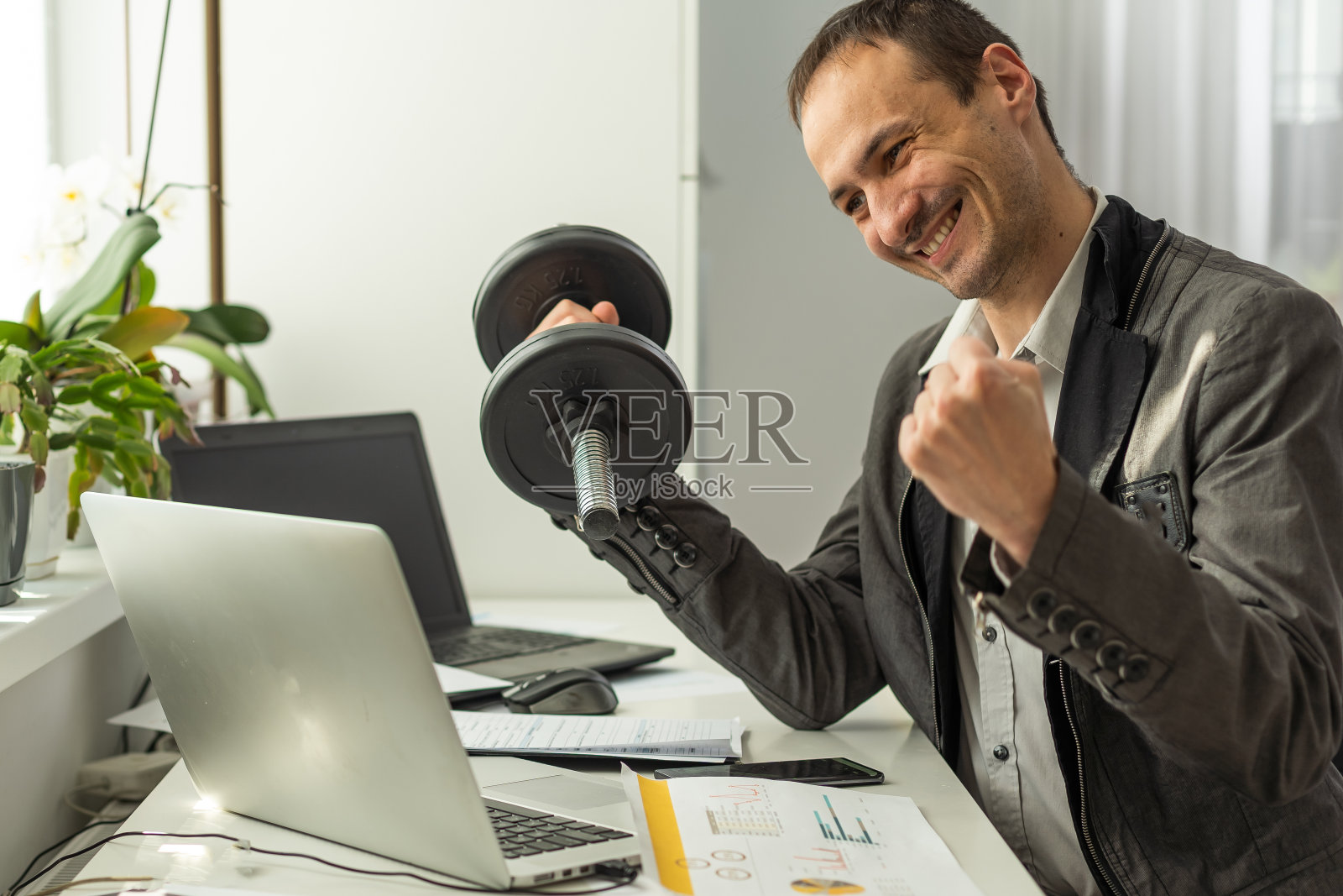 胜利的概念。一位成功、快乐、幸运、留着胡子的白人商人、公司首席执行官、经理，坐在办公室的办公桌前，用拳头打手势照片摄影图片