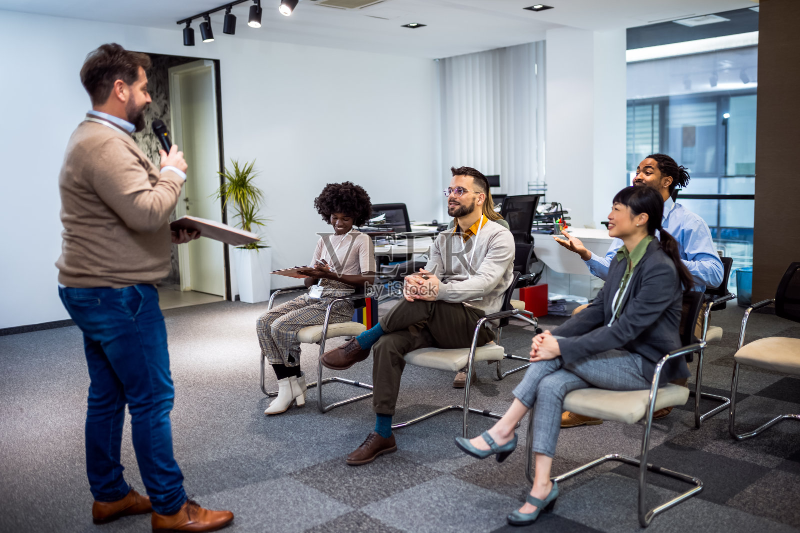 商人给他的多民族同事讲课。拿着麦克风讲话的。照片摄影图片