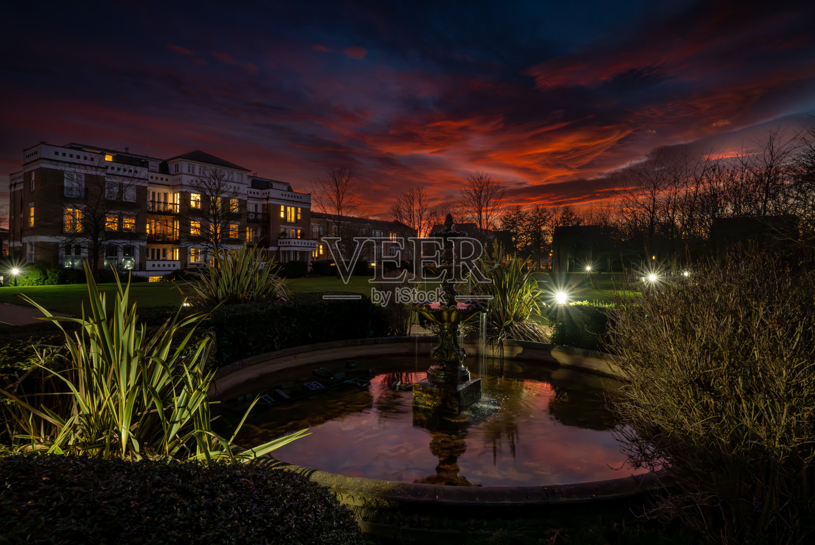 日落时公园里的喷泉和池塘，天空是红色的照片摄影图片