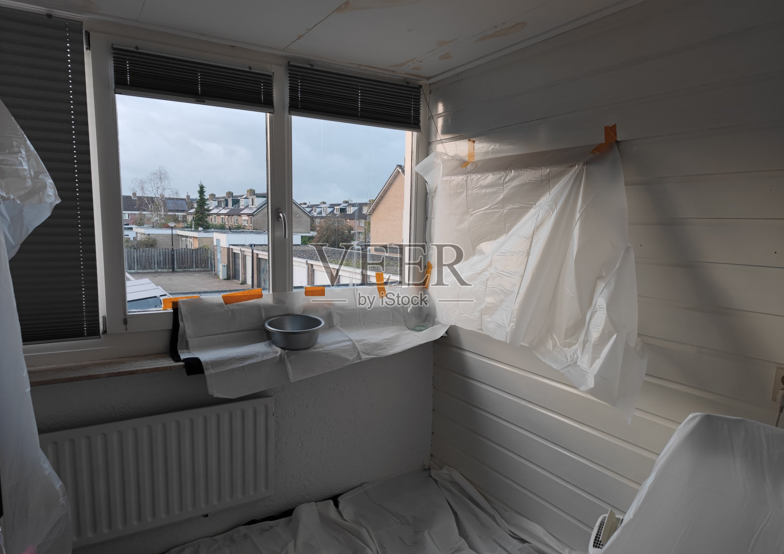 由于天花板和屋顶漏水，在一所房子的卧室里，窗台、墙壁、家具和悬挂物都被篷布覆盖照片摄影图片