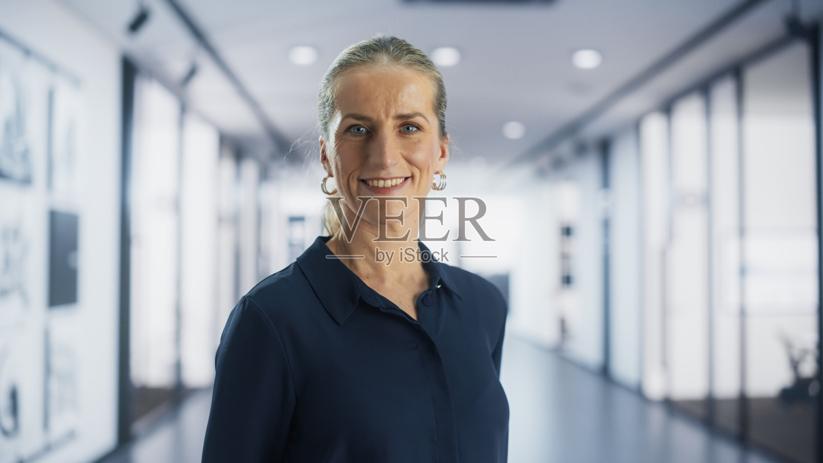 一个穿着西装的成年女性的肖像，微笑着对着镜头摆姿势。站在现代办公空间的白人女商人。授权CEO准备好管理一个成功的商业公司照片摄影图片