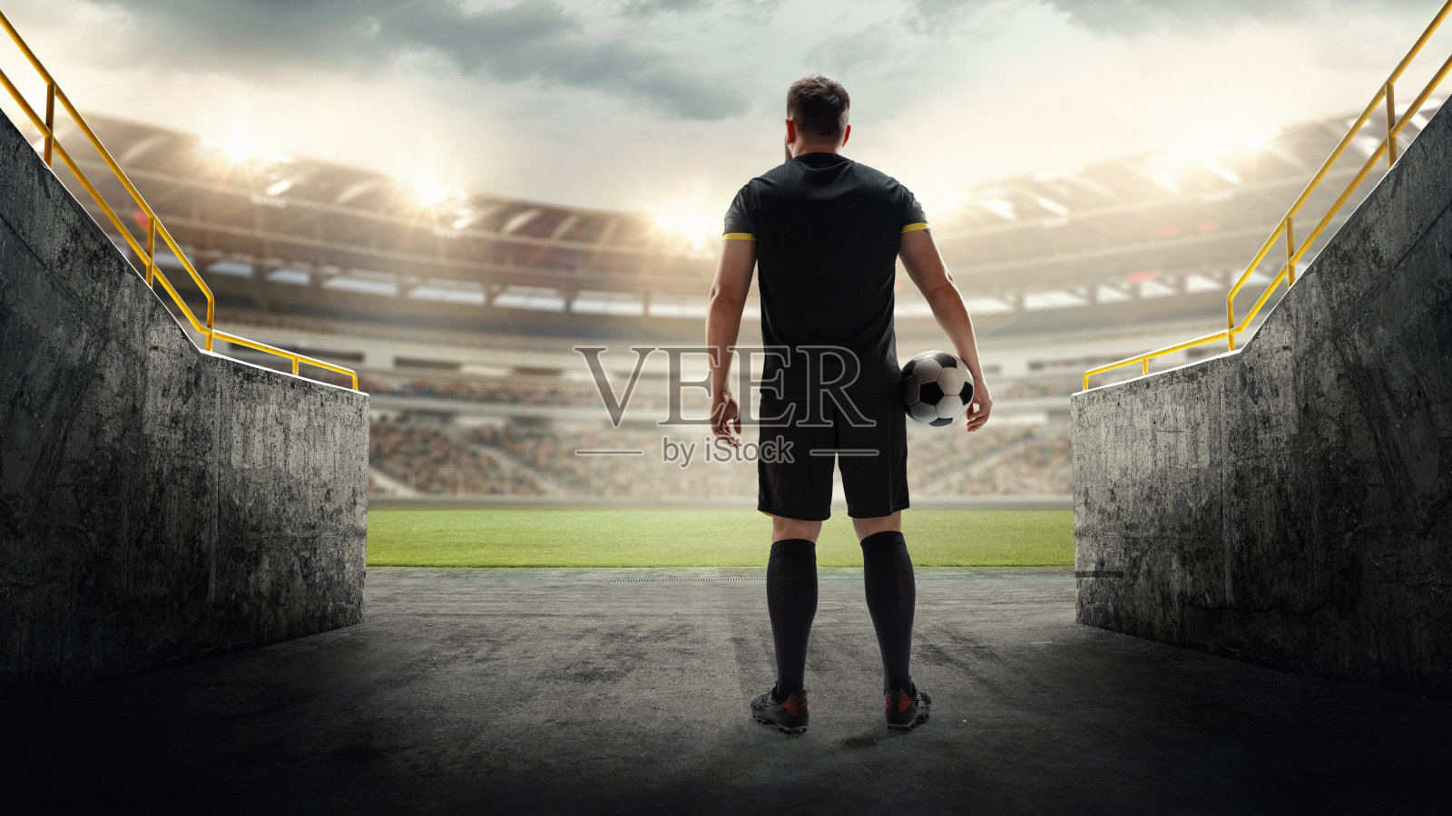 足球运动员站在入口处的球，看着空荡荡的3D体育场。激励运动员在大赛前表现出决心和期待。照片摄影图片