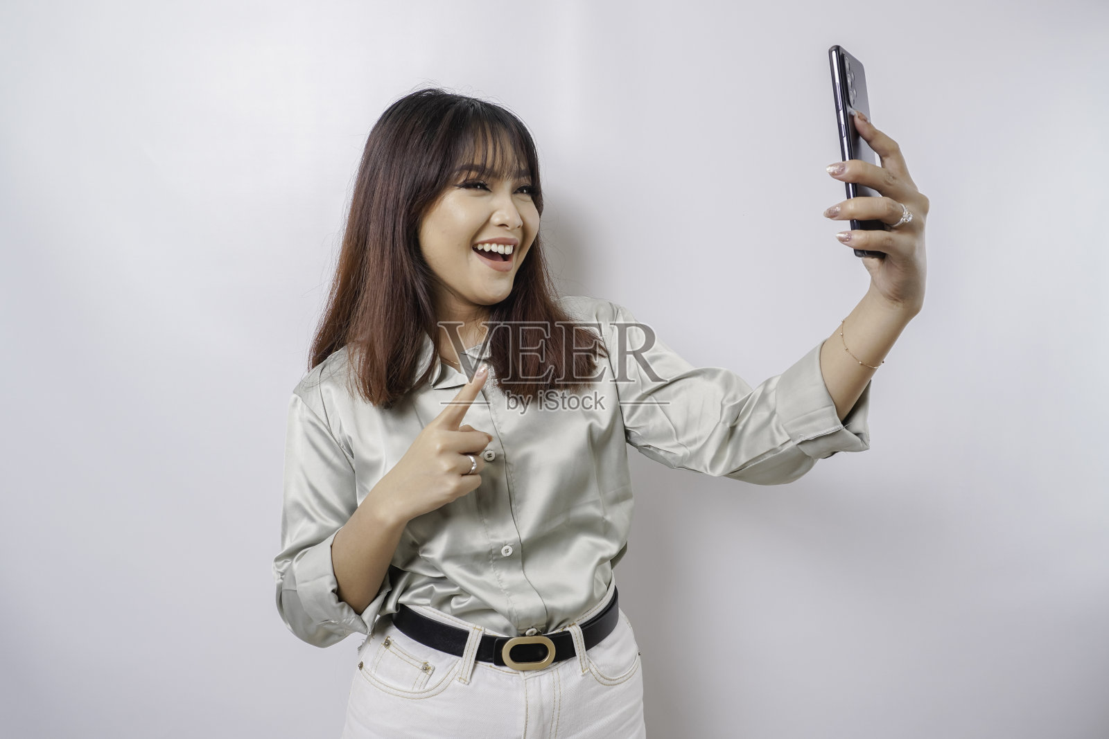 一个快乐的亚洲女人的肖像，穿着鼠尾草绿色的衬衫，拿着她的手机，被白色的背景隔开照片摄影图片