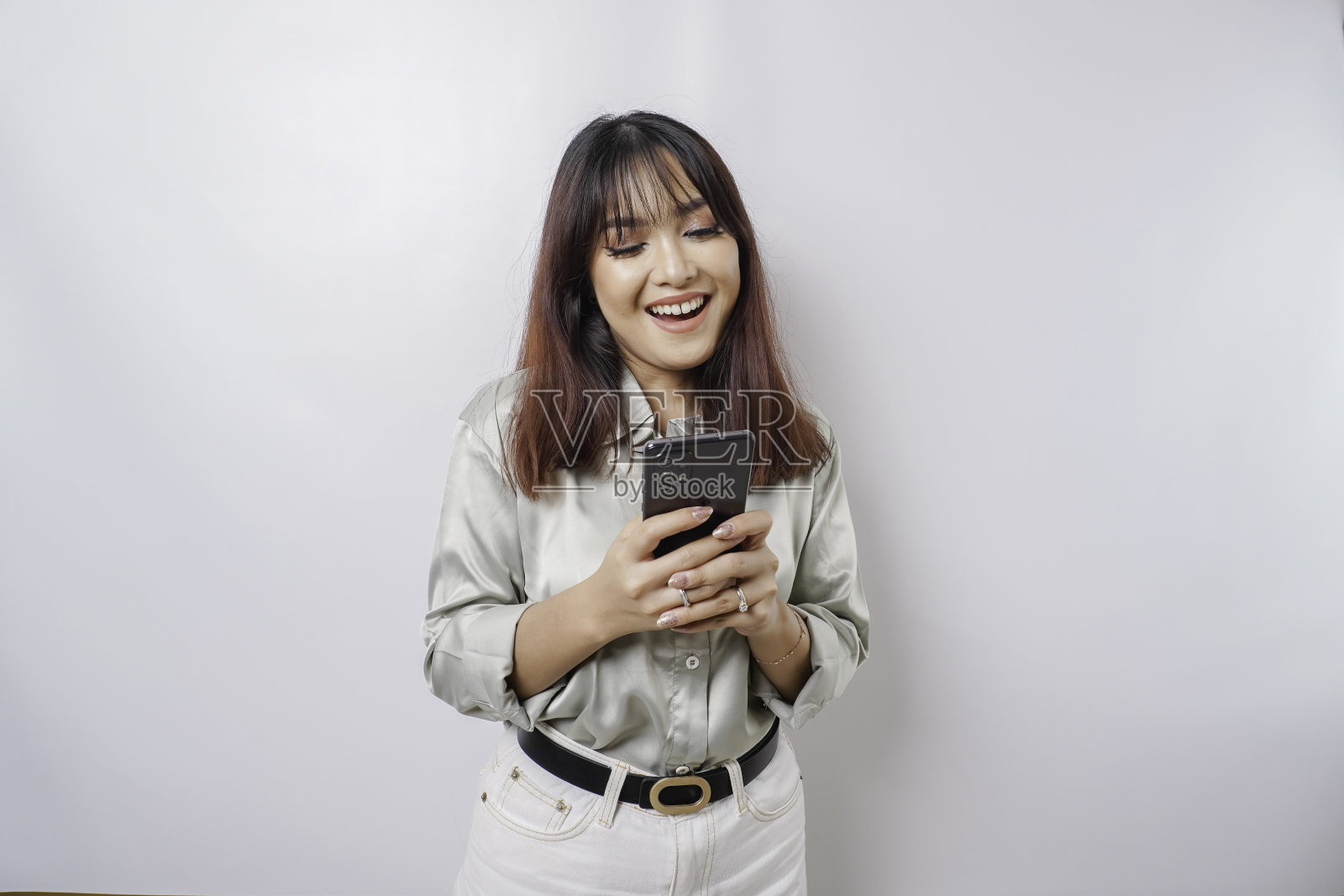 一个快乐的亚洲女人的肖像，穿着鼠尾草绿色的衬衫，拿着她的手机，被白色的背景隔开照片摄影图片