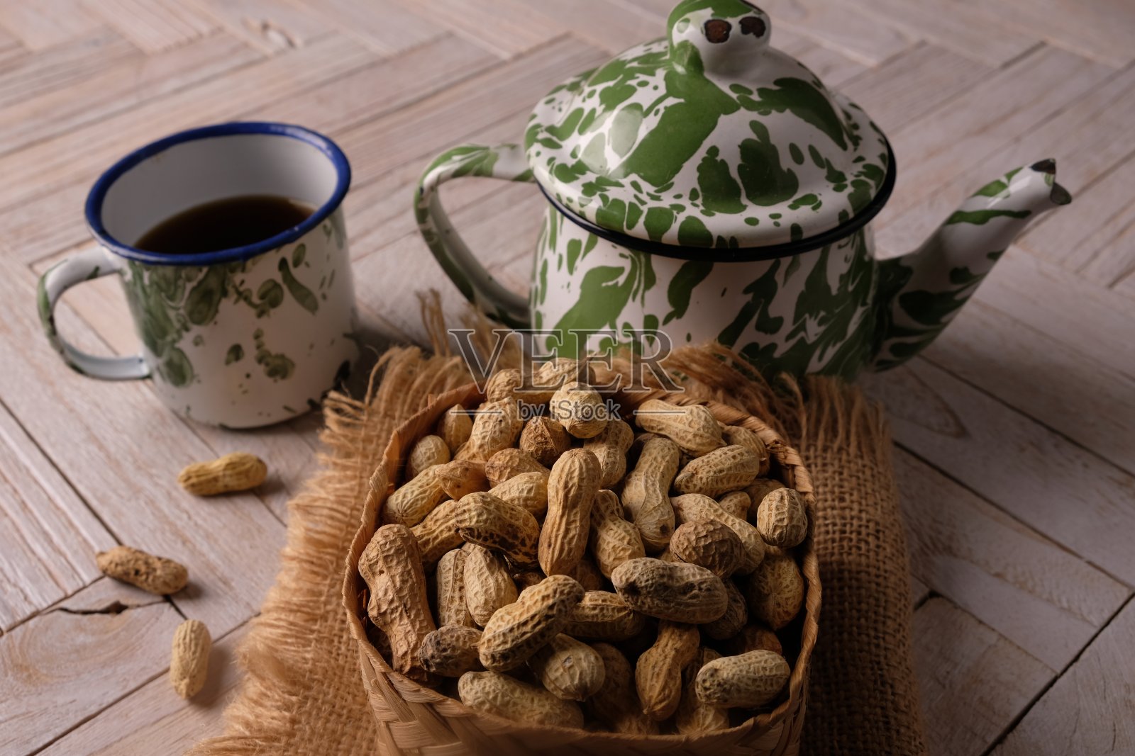 花生装在竹编容器里，放在木桌上。落花生hypogaea。一杯茶和一个茶壶。下午茶时间。照片摄影图片