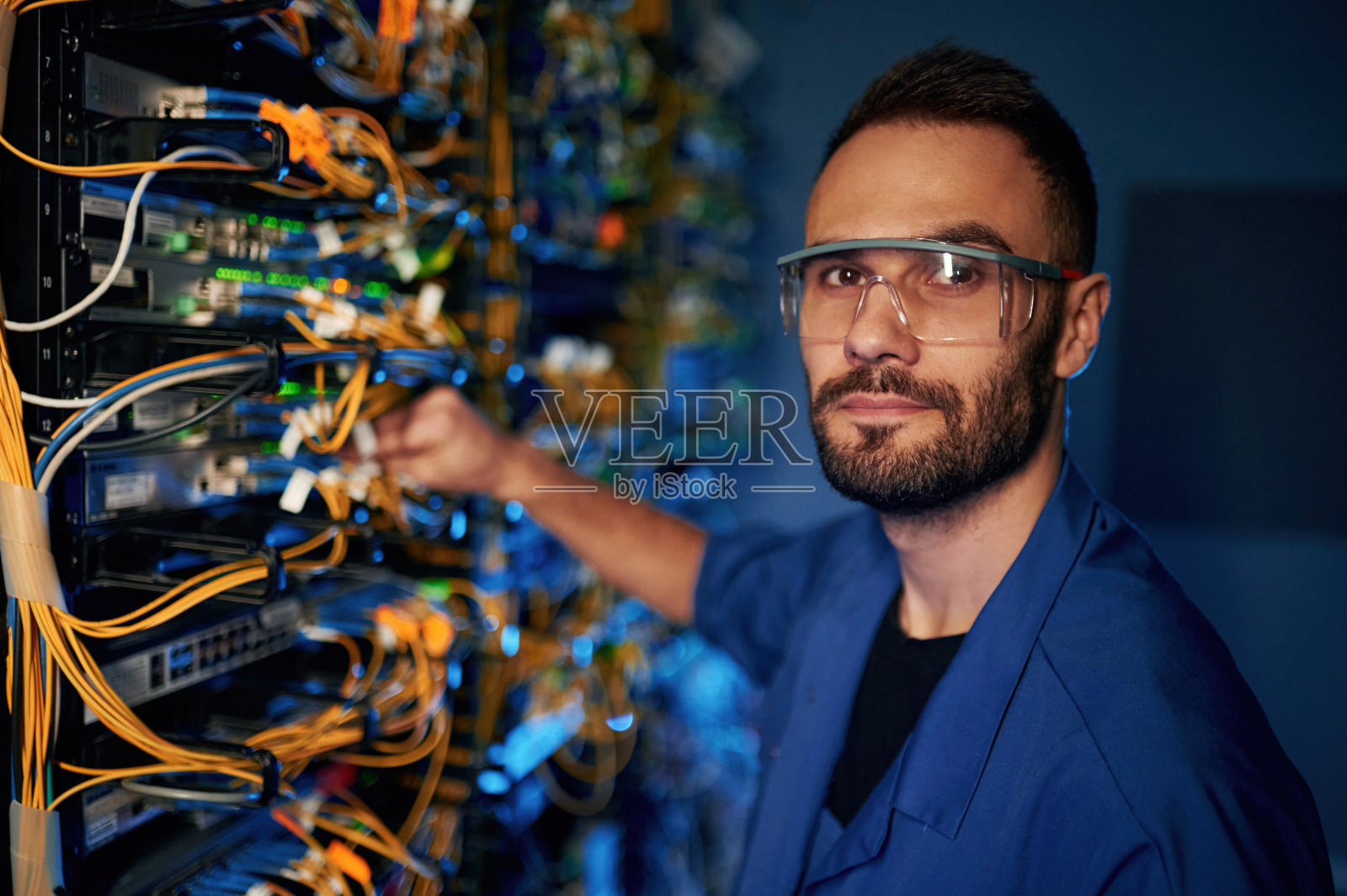 看着镜头。年轻人正在服务器机房里摆弄网络设备和电线照片摄影图片