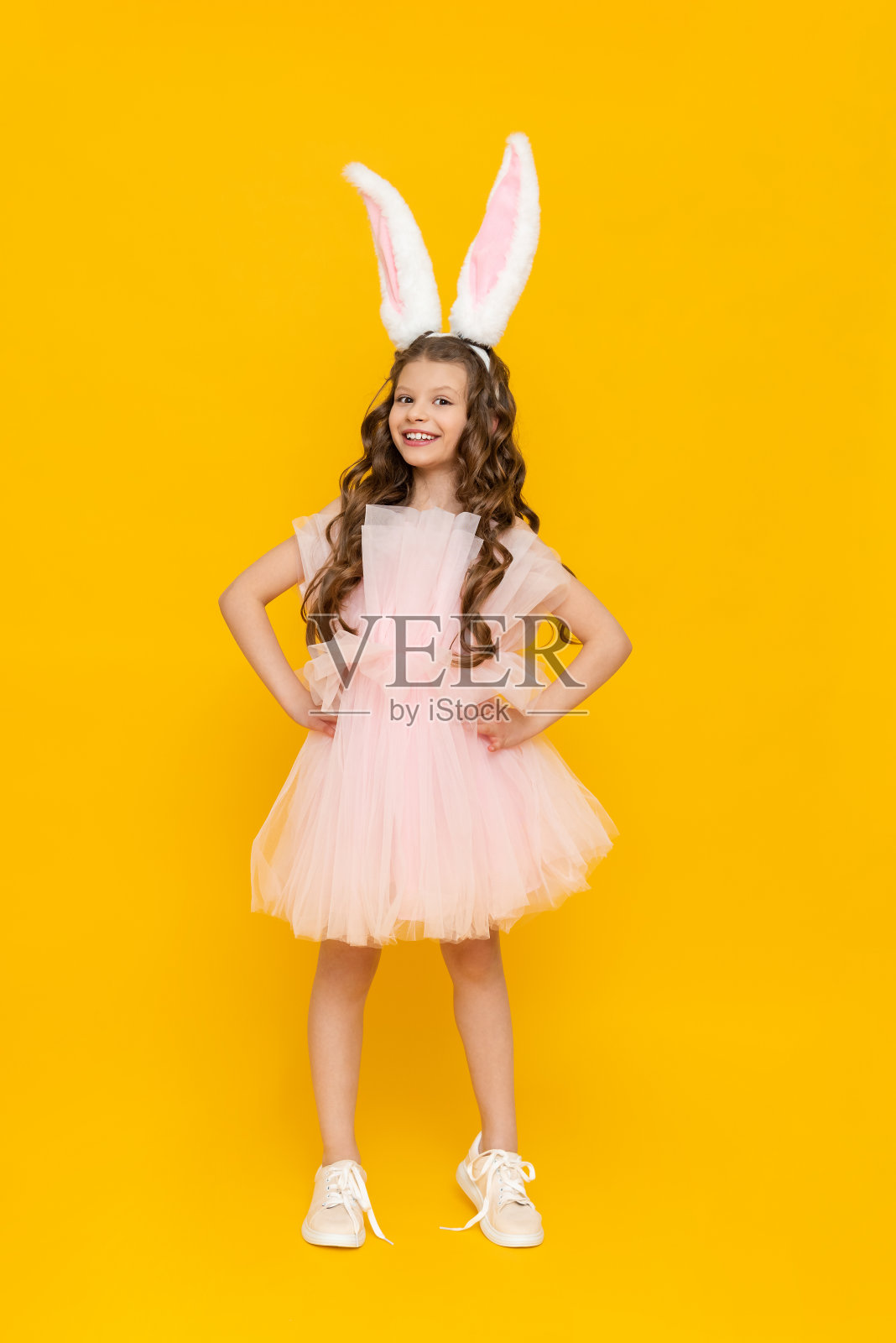 复活节是孩子们的节日。一个十几岁的女孩穿着华丽的衣服，在春天里欢欣鼓舞。这个孩子戴着长长的兔耳。一个美丽的小女孩，一头长发，在黄色孤立的背景上照片摄影图片