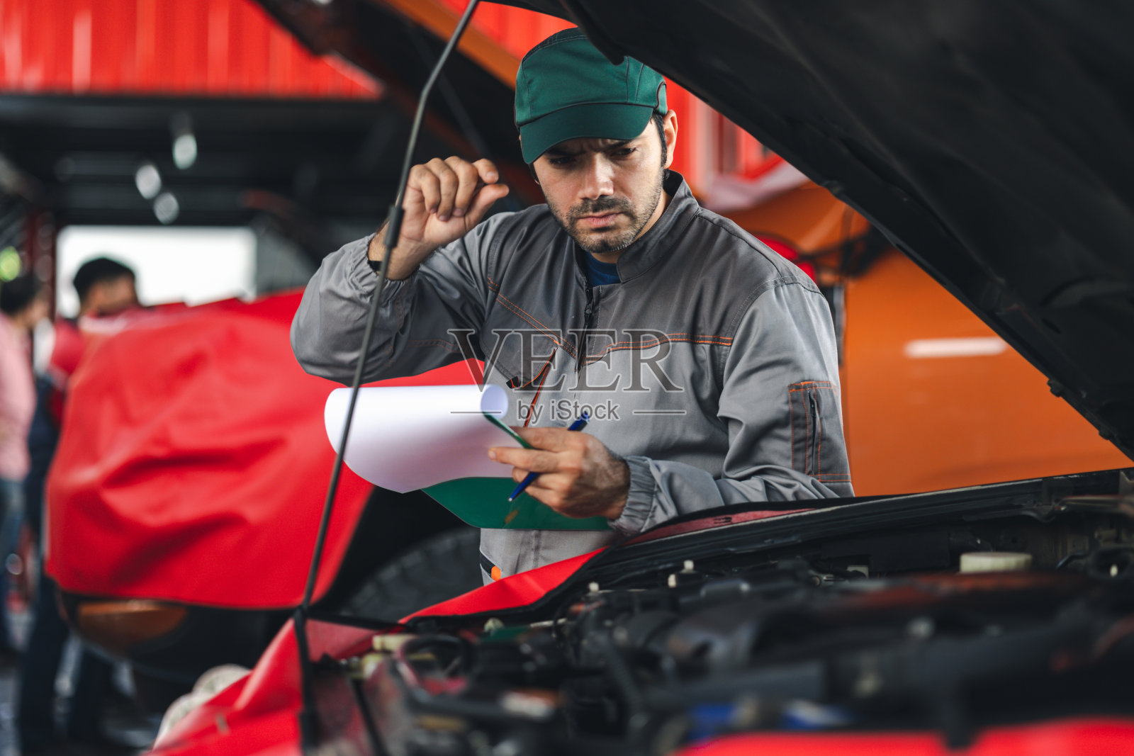 专业的汽车维修人员用剪贴板检查汽车损坏部件的状况。在汽车修理厂诊断和修理车辆。照片摄影图片